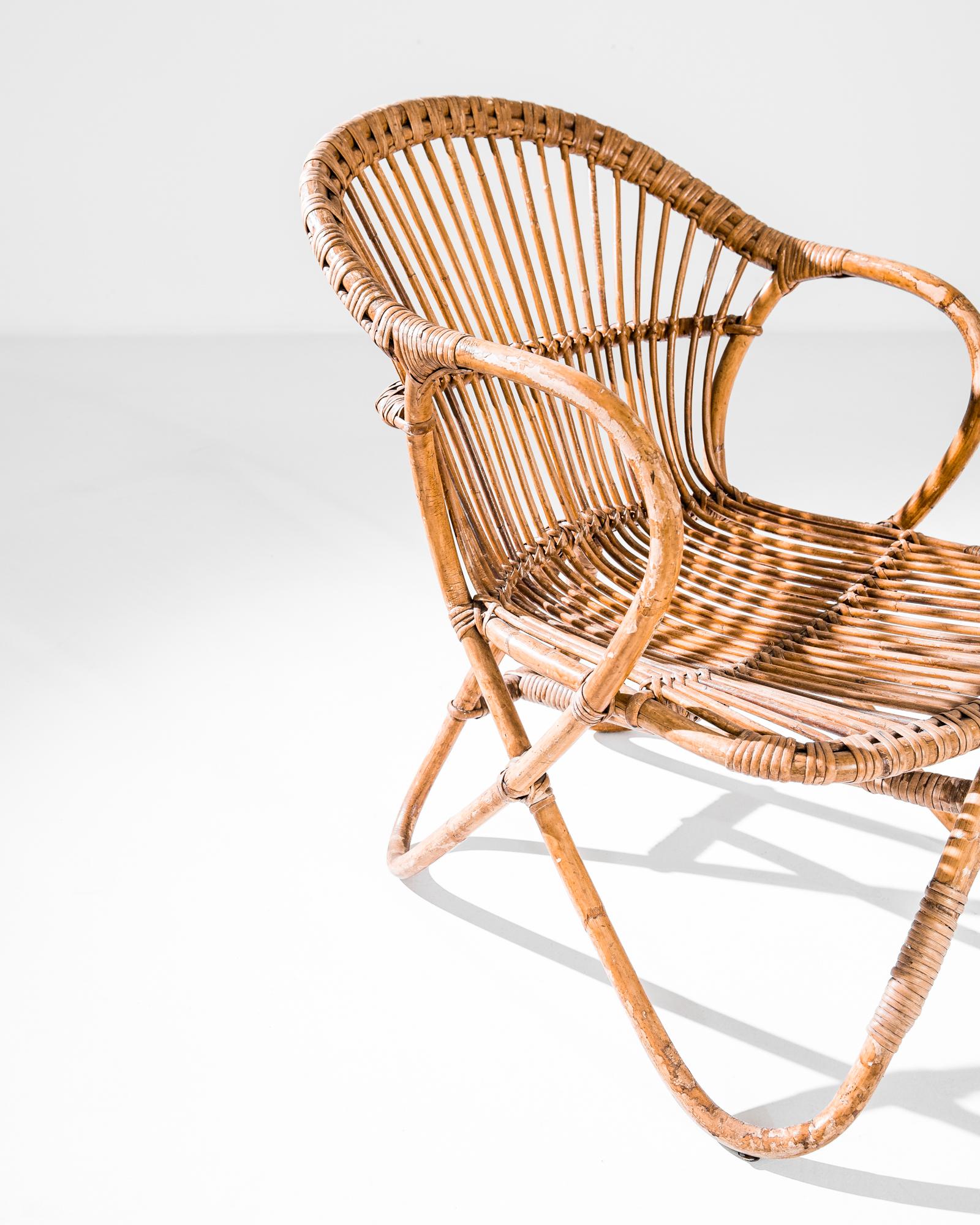 A bamboo armchair from 1960s France. The honeyed tone and natural lightness of the rattan vine gift the frame an airiness and warmth. Hand-woven detail adds a homey, organic accent. The curves of the looping arms and deep circular seat create a