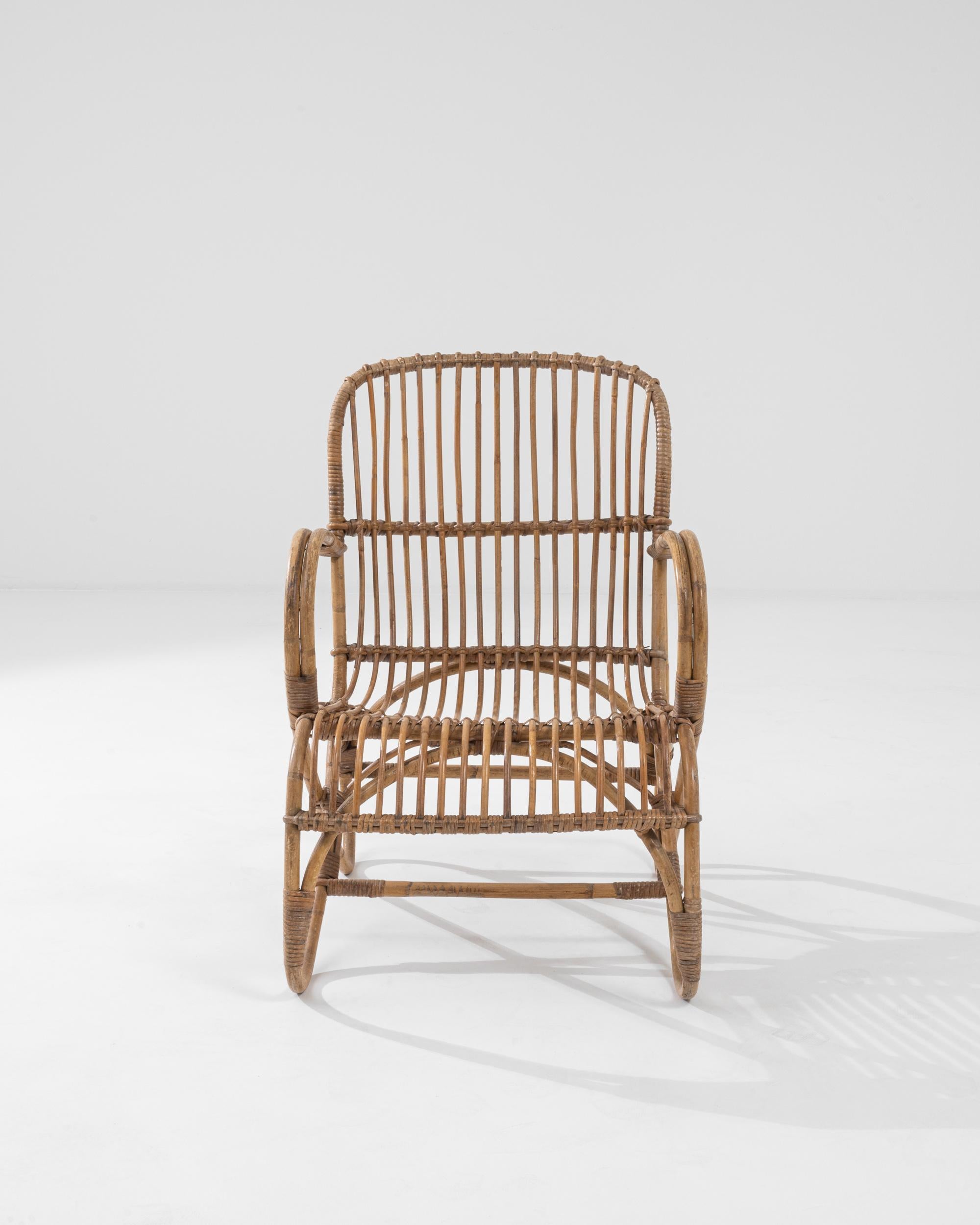 A wooden armchair from 1960 France. This french-made armchair is a playful twist on a mid-century classic. Using lashed together rattan, artisans have crafted a chair both geometrically pleasing and surprisingly comfortable. Created by looping