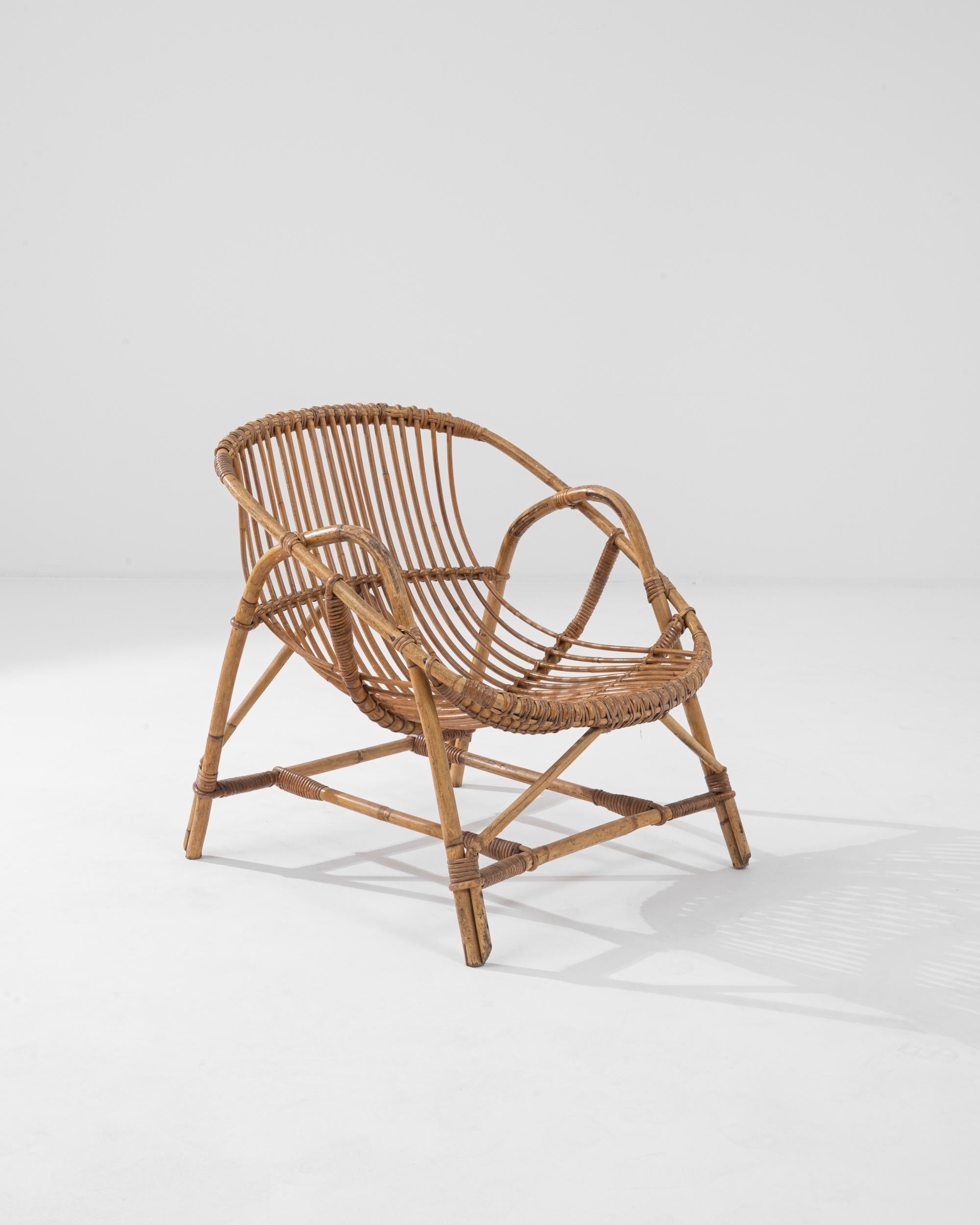 A wooden armchair from France, circa 1960. This french-made armchair is a playful twist on a midcentury classic. Using lashed together rattan, artisans have crafted a chair both geometrically pleasing and surprisingly comfortable. Created by looping