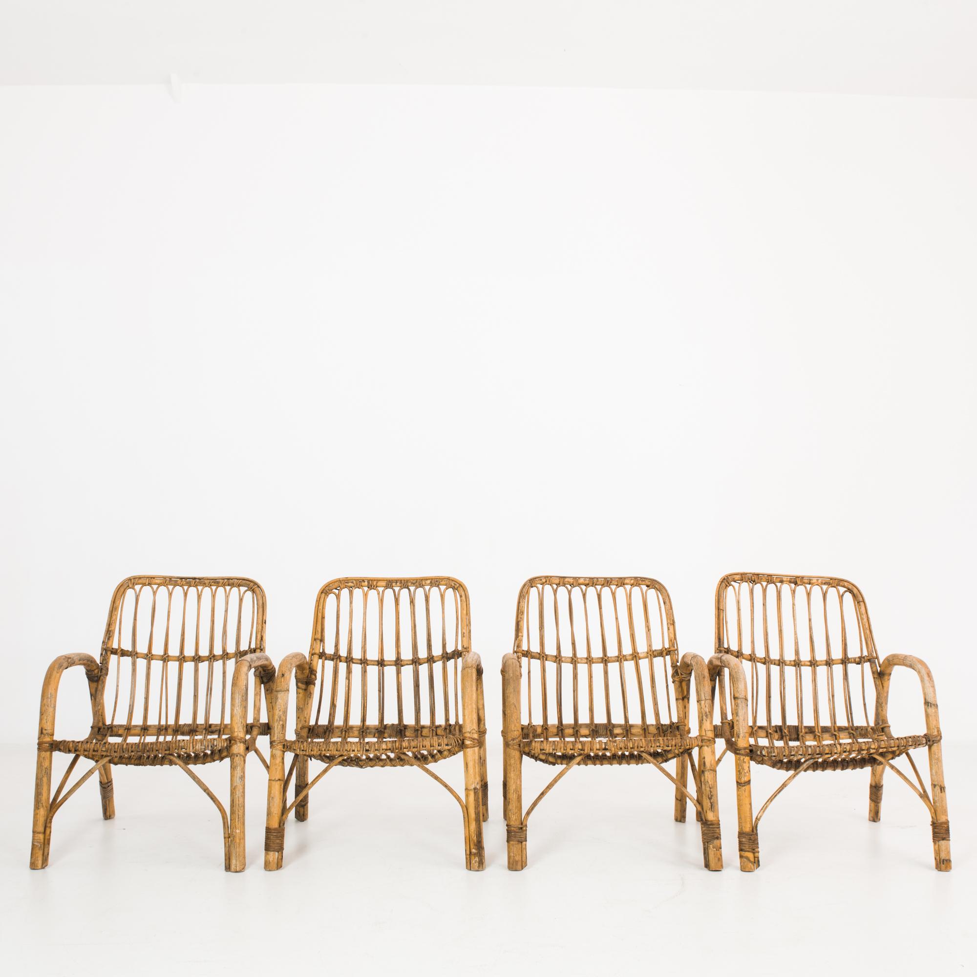 This set of rattan armchairs was made in France, circa 1960. The strength and beauty of the material are on display in its elegant construction. A single stem is bent to form the armrest and legs on each side, while canes are shaped into a gently