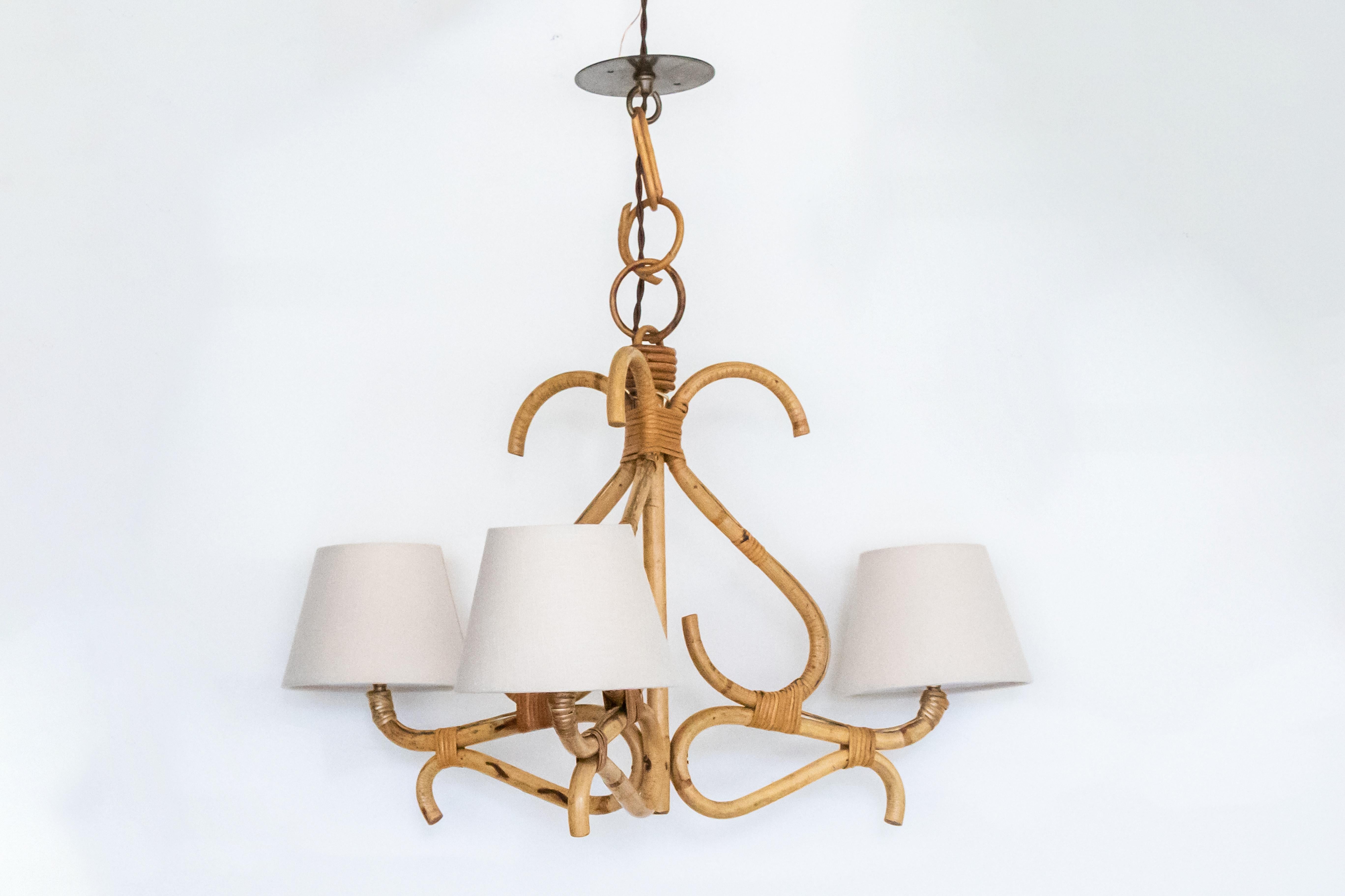 French rattan chandelier with three lights. Original rattan in decorative shape and original finish. Newly re-wired and new linen shades. 

Measures: Overall height 24.25