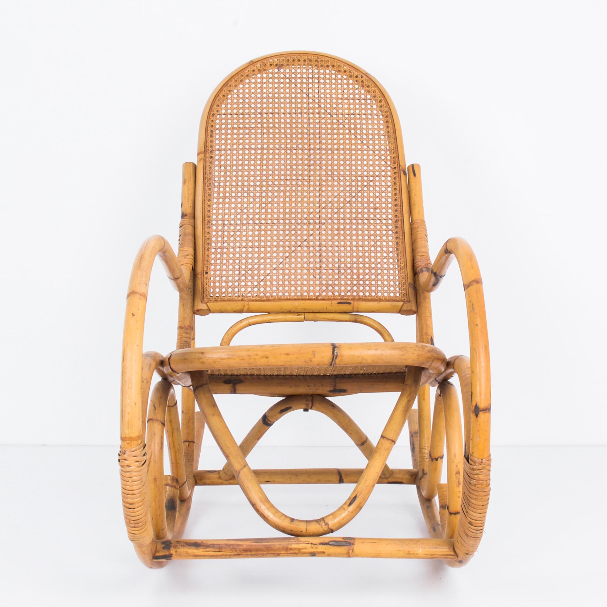 This rocking chair was made in France, circa 1960. Made of rattan, the chair reflects the Indochine style of using natural materials to update the bentwood rocking chairs produced in Europe from the late 19th century-- a reference to makers the