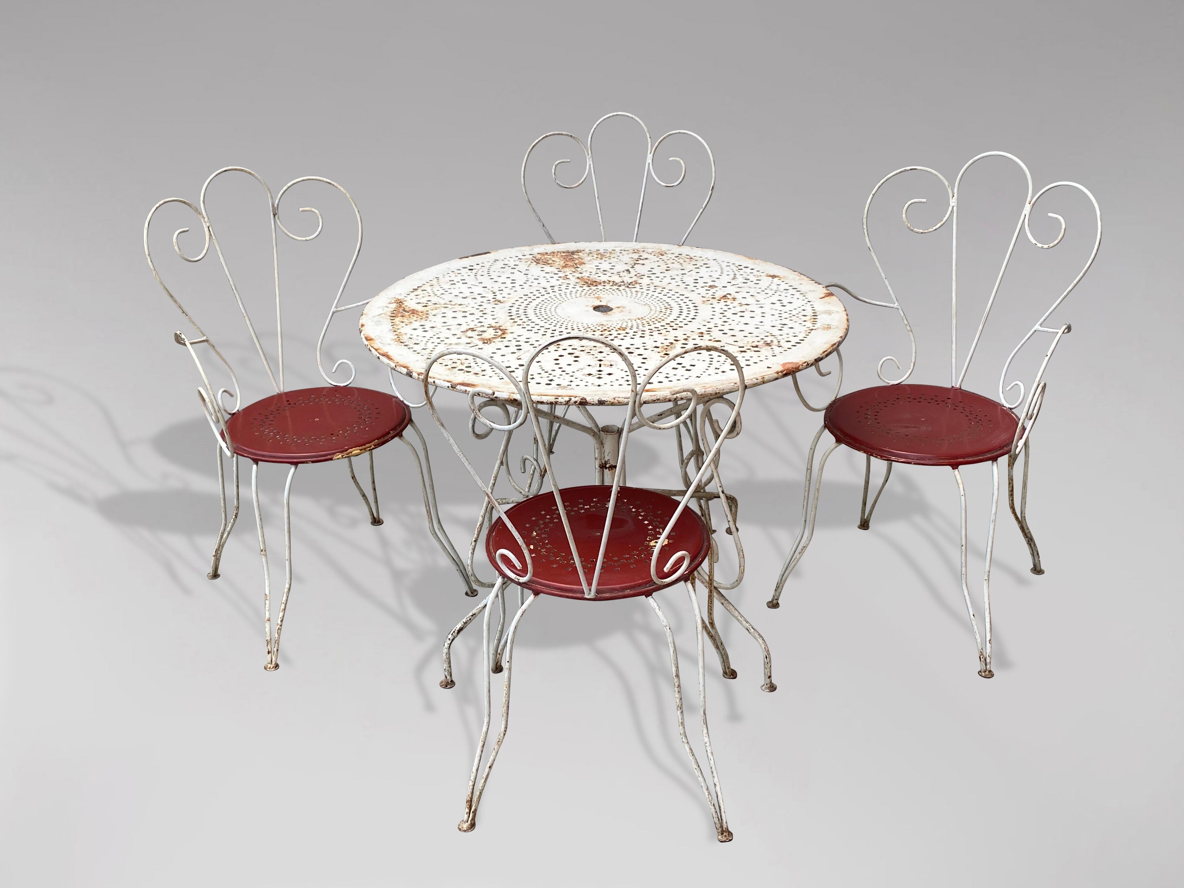 A mid 20th century French Riviera, original white painted wrought iron outdoor setting of classic design comprising the original fretted metal top round table and its 2 chairs and 2 armchairs. The chairs have wrap around backs and red painted