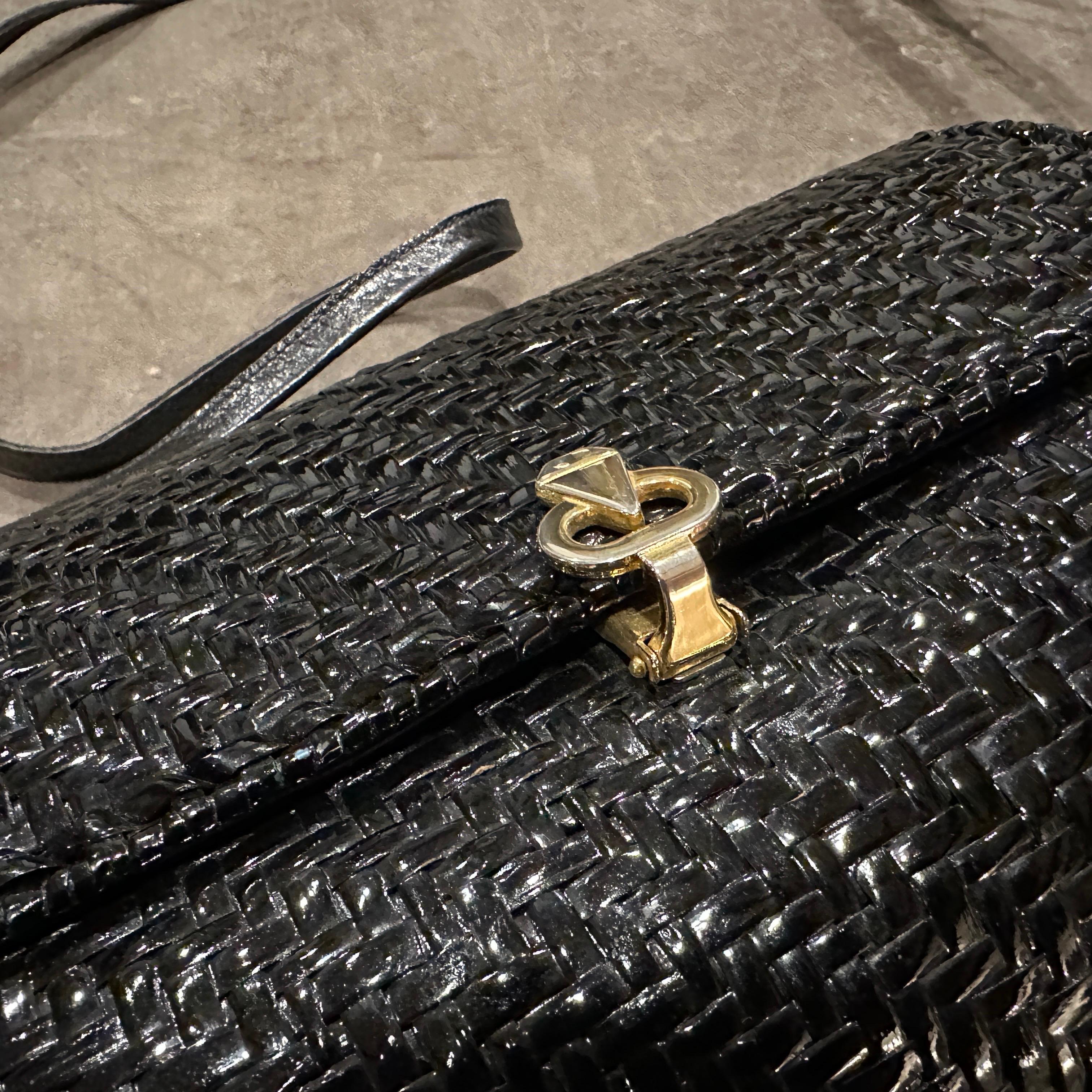 This Italian vintage shoulder bag is a striking blend of elegant texture and mid-century charm, combining traditional materials with a refined silhouette. The bag is crafted from glossy black wicker, woven in a tight, intricate pattern that gives it