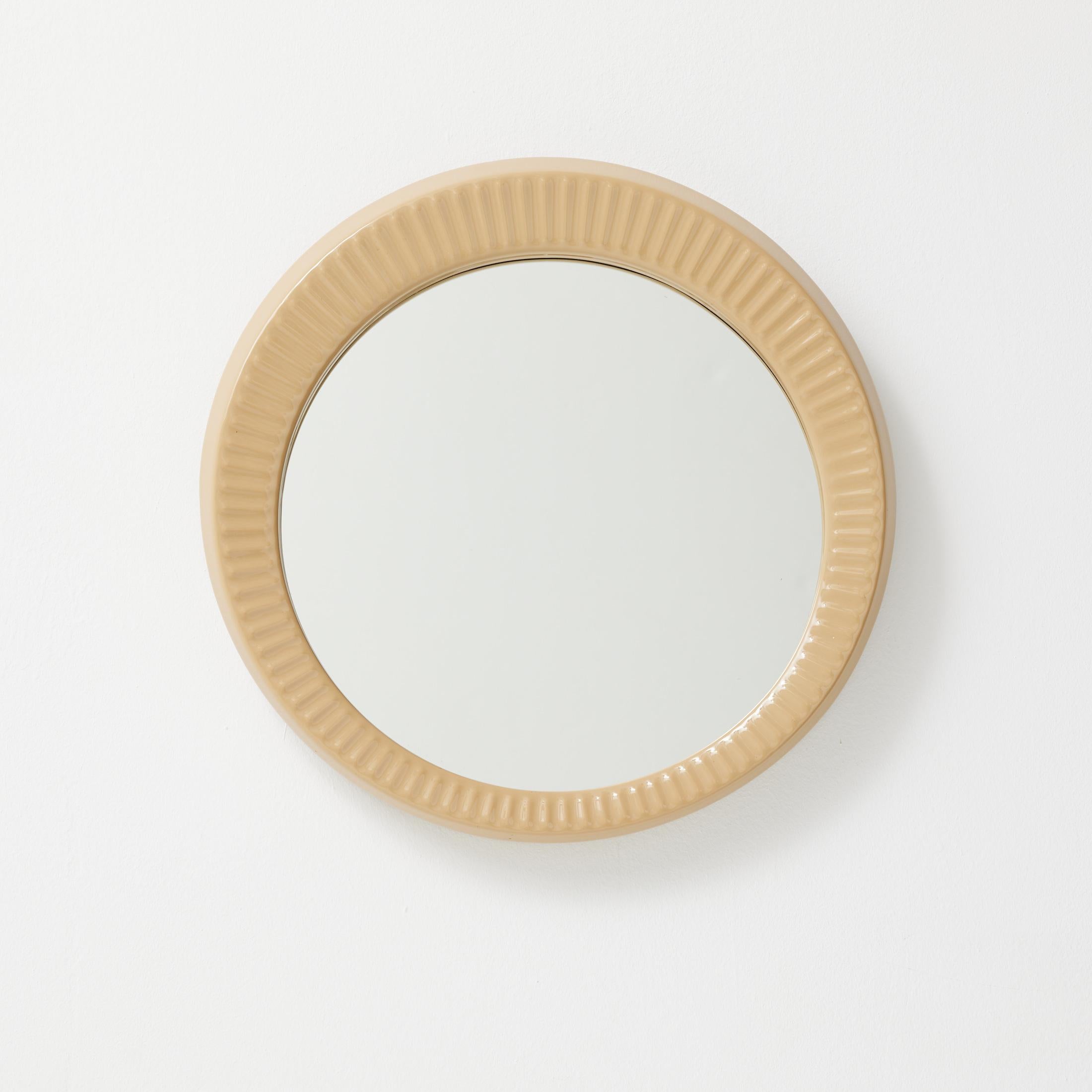 An eye-catching French wall mirror from the 1960s, featuring a round ceramic frame with vertical fluting and a warm glazed beige tone. Its sculptural ridged texture gives the piece a sense of rhythm and tactility, while the soft gloss of the ceramic