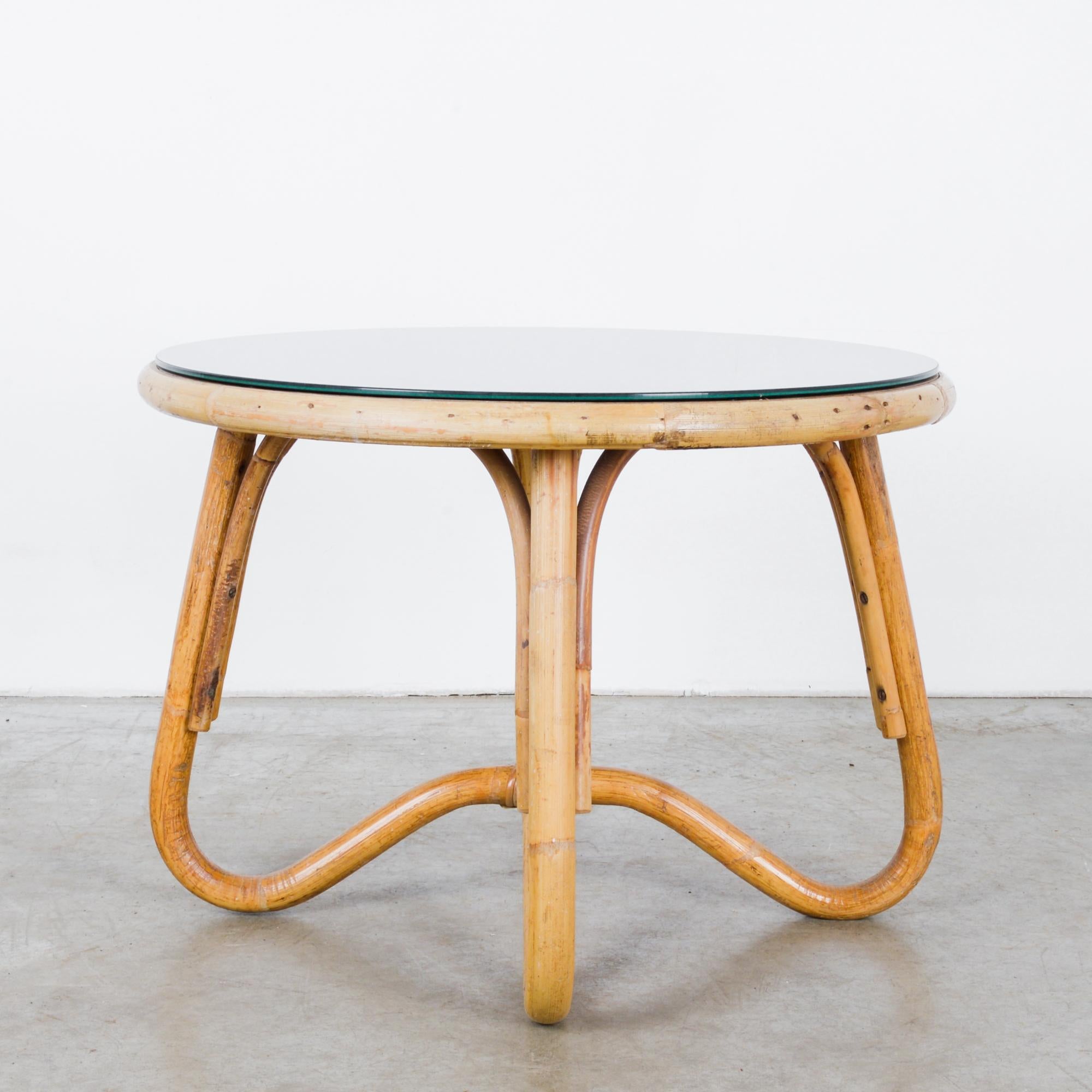A round bamboo table with a black glass top from France, circa 1960. The supple shape makes inspired use of the natural pliability of bamboo; the legs loop and unite beneath the center of the tabletop, giving a Mobius effect of an unbroken line. The