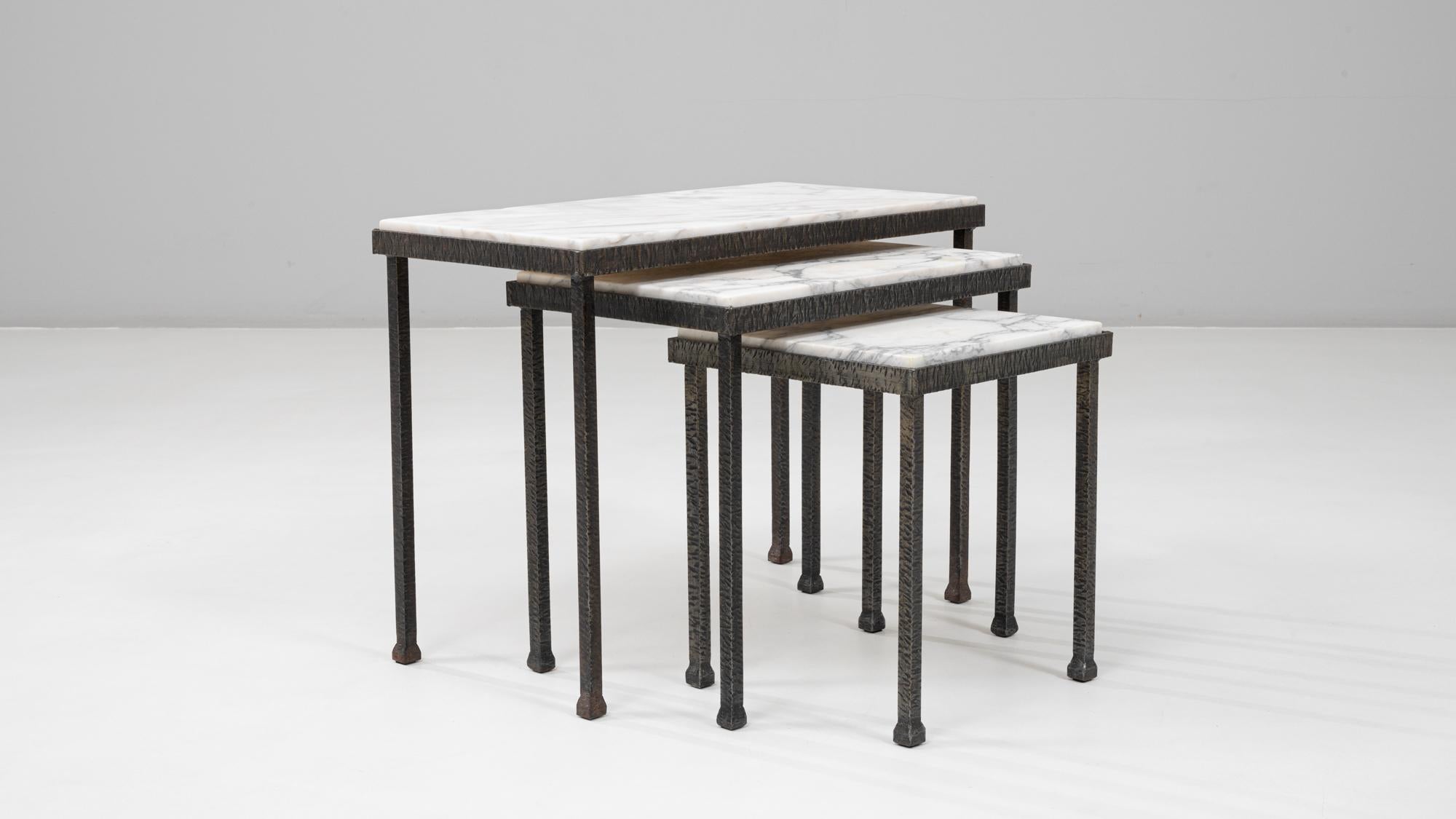 Questo set di tre tavolini a nido francese degli anni '60 combina una scultorea lavorazione del ferro con raffinate superfici in marmo. Ogni tavolo presenta una struttura in ferro con dettagli cesellati e gambe sottili, che conferiscono un senso di
