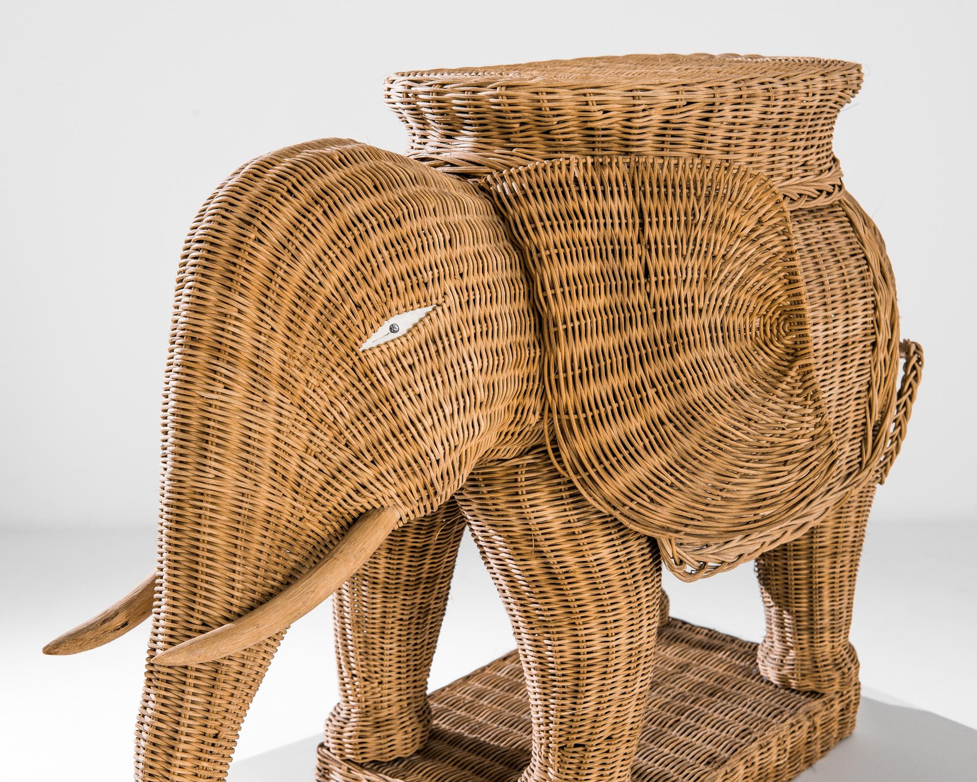 A wicker elephant from France, produced circa 1960. Measuring just under two feet tall, this woven sculpture is a monument in miniature to a king of the jungle. As it stands ready to ride, wrapped in a blanket and mounted with a howdah, or elephant
