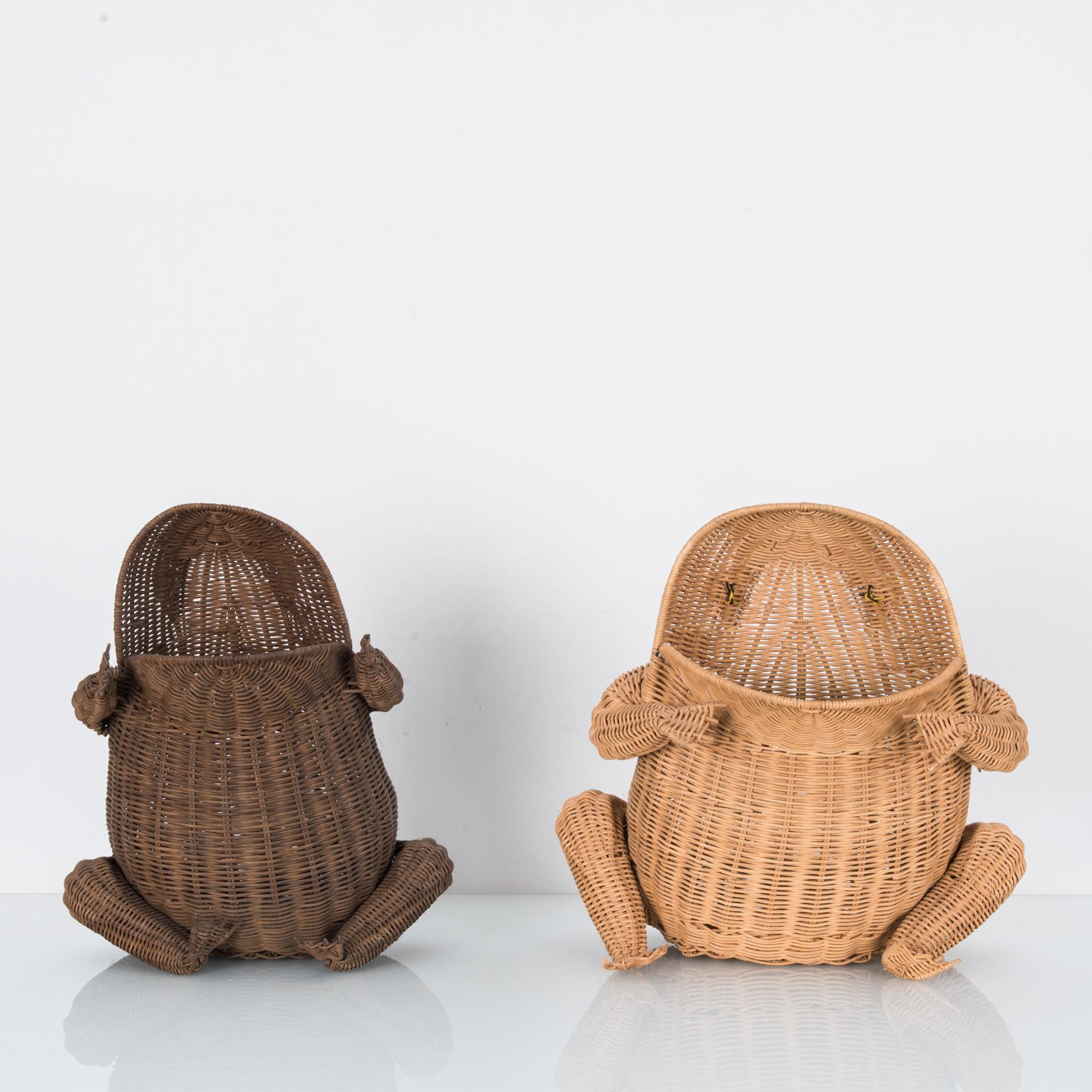 A pair of wicker frog baskets from France, circa 1960. Two frogs, one woven in dark cane, one in light, sit with their arms outstretched and mouths open wide. The opening of the mouth creates the opening of the basket, items can be stored in the