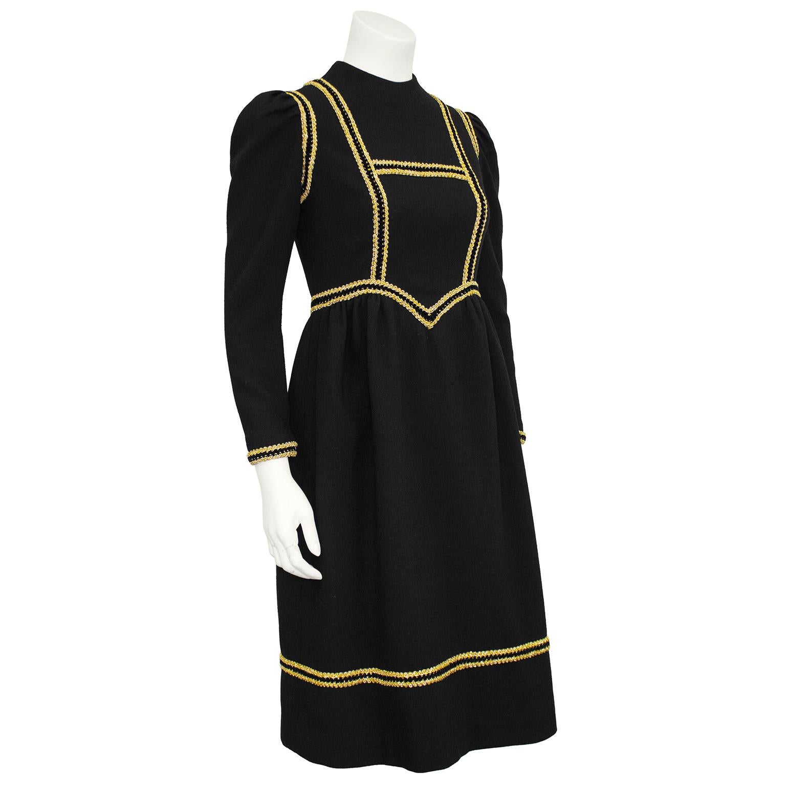 Vestido de inspiración renacentista de los años 60 de Geoffrey Beene. Lana negra con ribete dorado grueso en contraste en todo el corpiño y en los puños y el bajo. Cuello mao con mangas largas de cordero y entallado en todo el cuerpo con falda midi