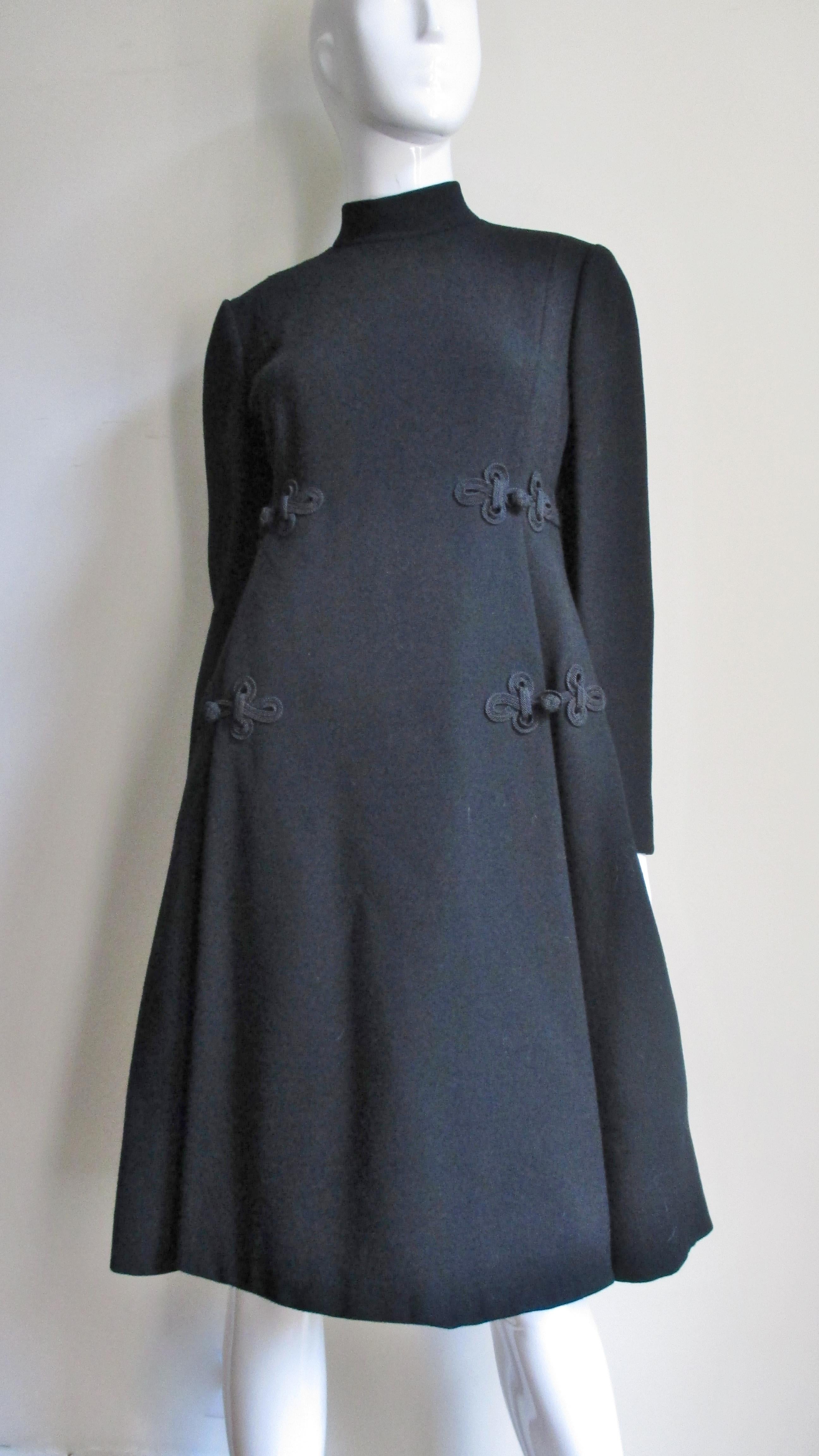 A fabulous rich black wool dress from Geoffrey Beene. It has long sleeves, a small stand up collar and and an inverted fold on either side of the center front. There are detailed silk braided frogs with knots at the side upper and lower waist level.