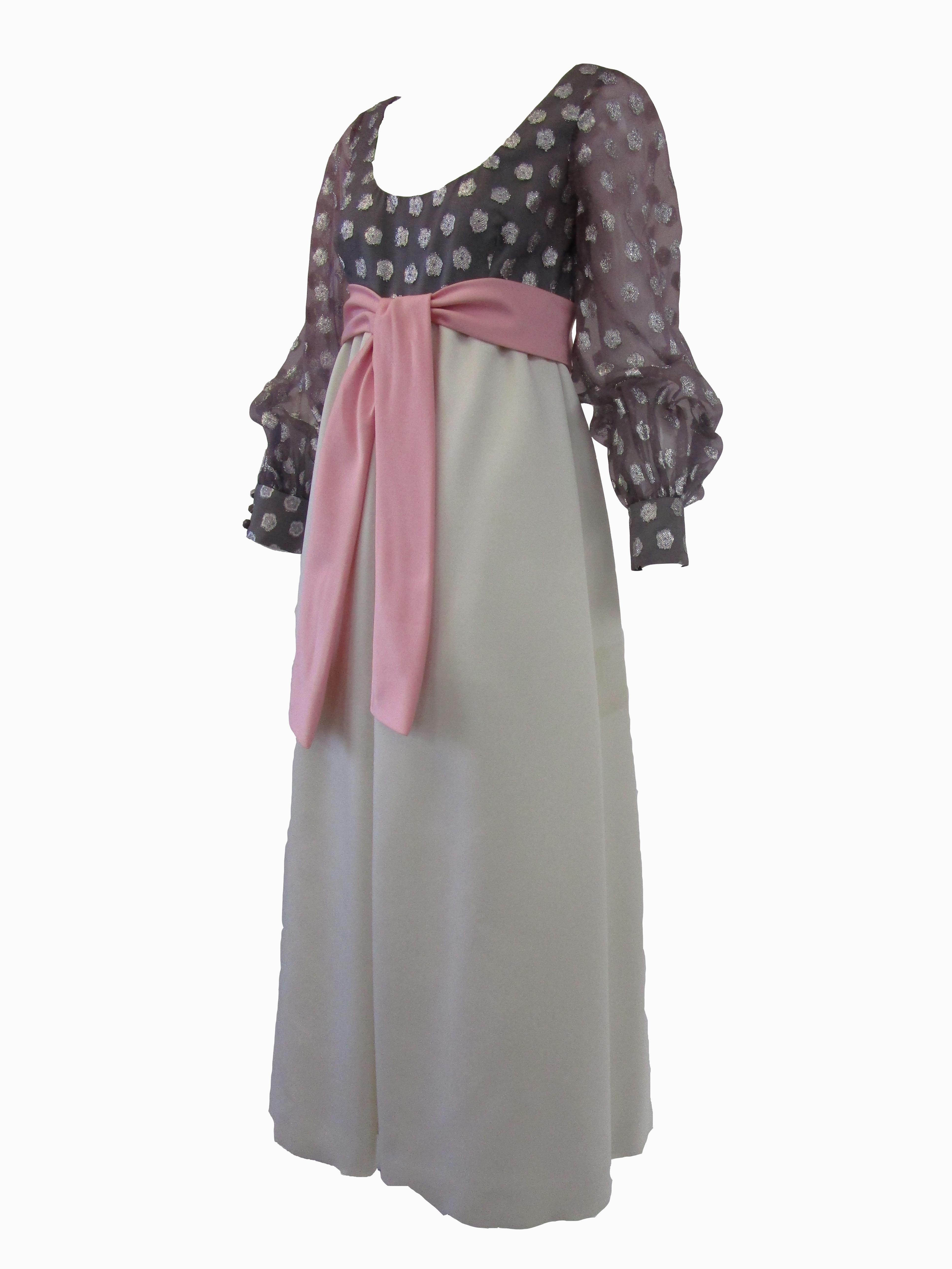 Youthful & fun scoop neck evening gown done in a sheer metallic polka dot over silk with a pink bow belt. Silk satin gathered skirt is an off white. Sheer sleeves button at cuff. Zips at back. All lined in silk.

Geoffrey Beene began his career in