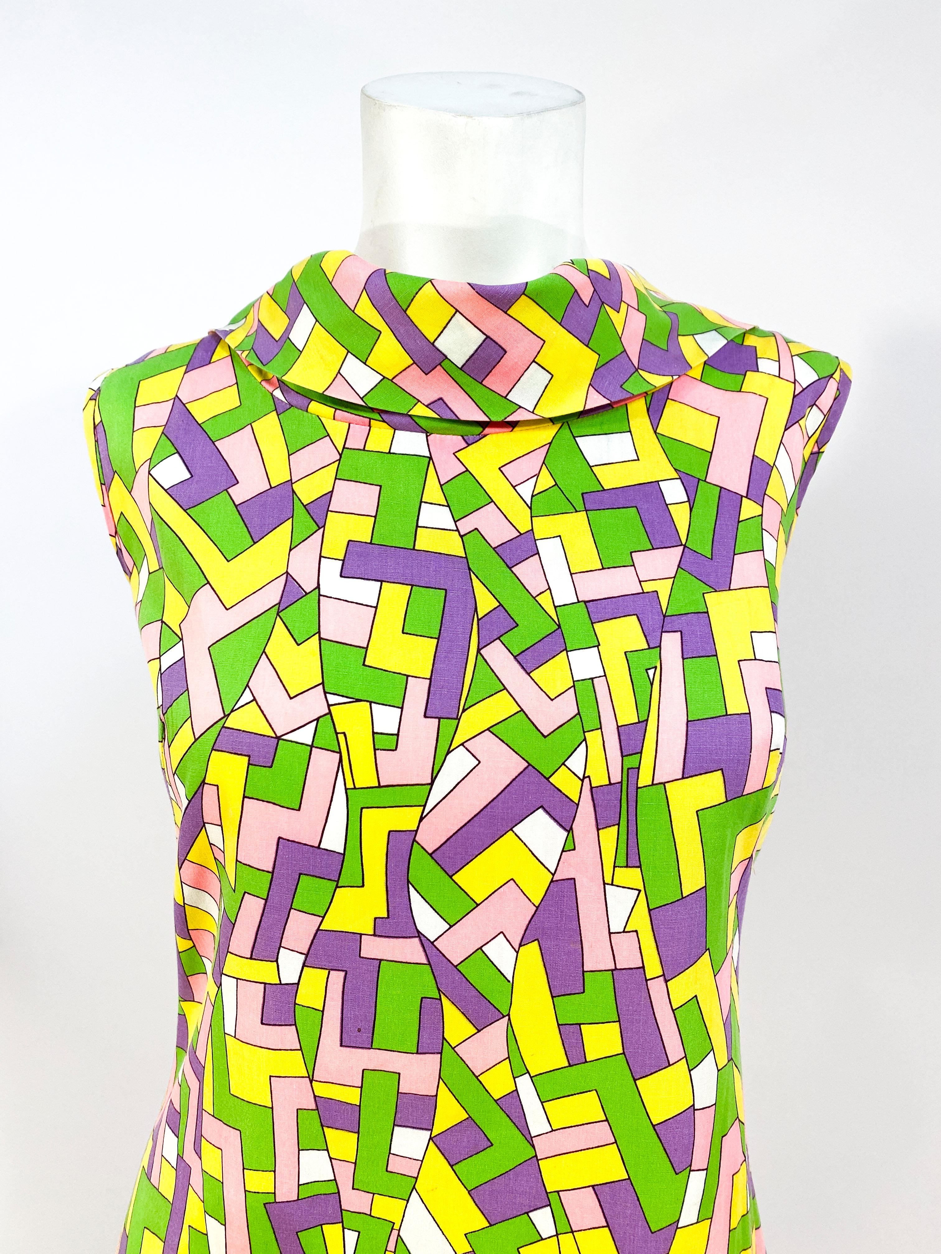1960s Geometric in yellow green, and purple printed scort dress with boat/turtle neckline, that is sleeveless, has piped trimming, and an A-line silhouette.  Note that this dress has a crotch that is hidden with the drape of the full pant/short