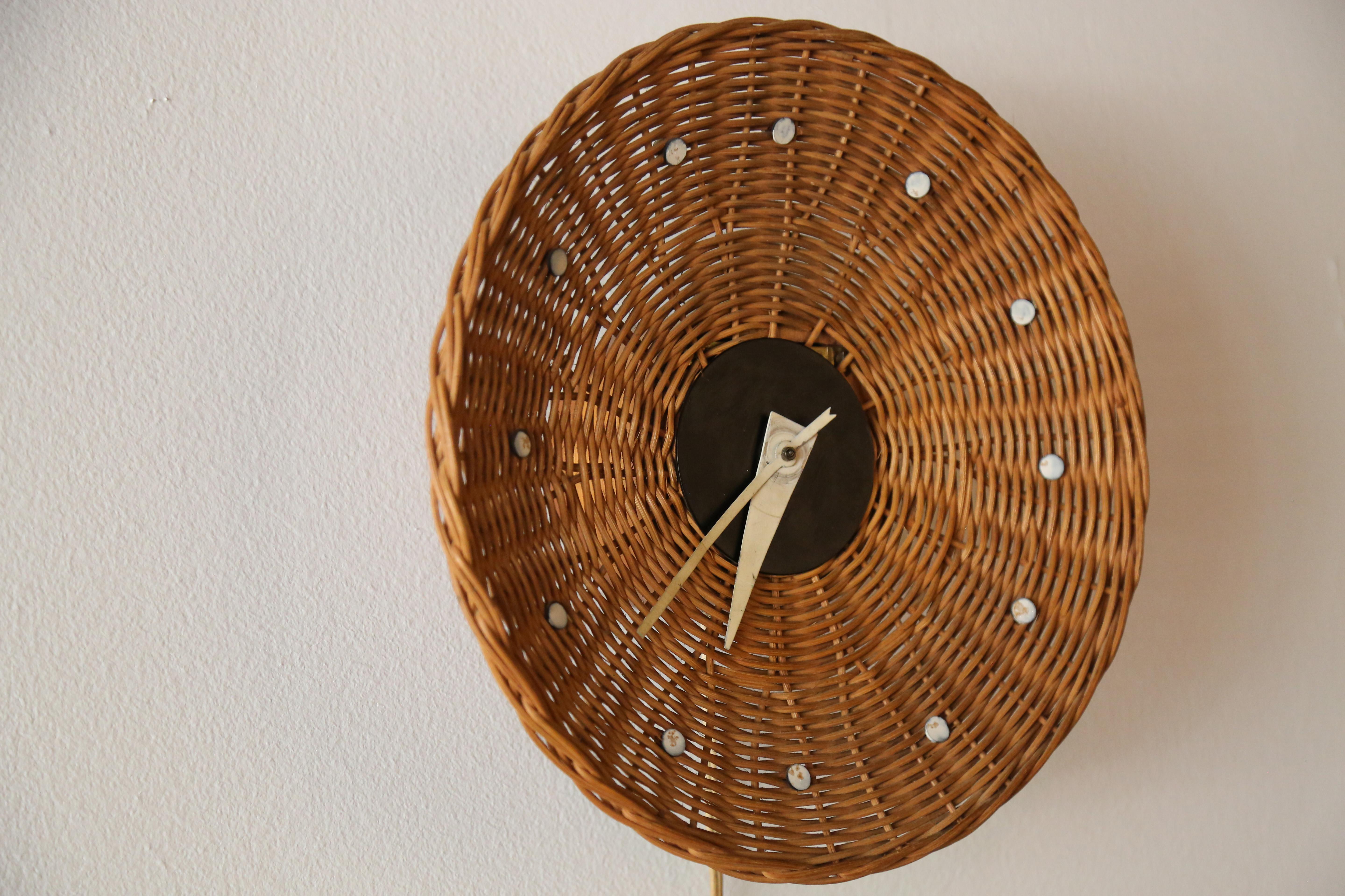 Iconic clock designed by George Nelson for Howard Miller. Model #2215 Basket clock for Howard Miller combines mid century modern with a great textural look. The woven basket, adorned with 12 metal discs, suspends off a thick Birch Base which adds