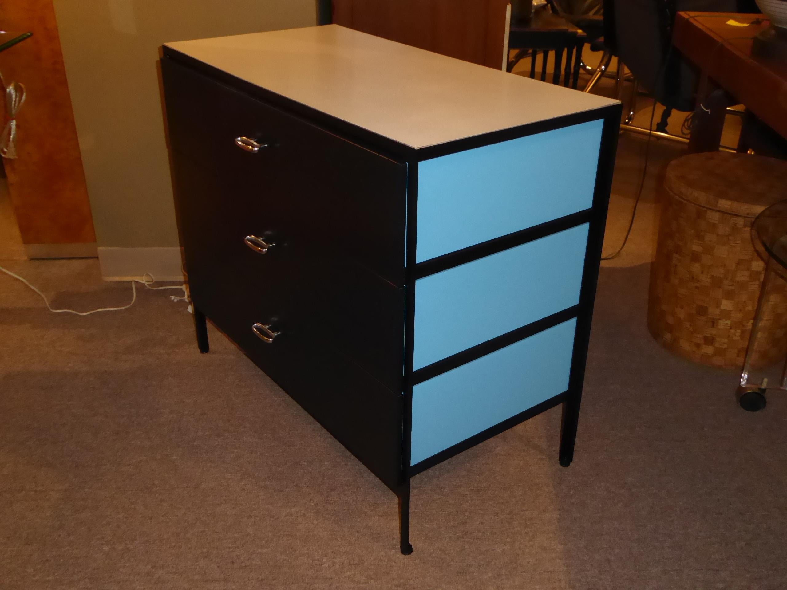 Quite nice steel frame dresser by George Nelson for Herman Miller consisting of a white mica top and three drawers with black painted fronts and Royal blue painted sides and back that show through the open blackened steel frame design. Each drawer