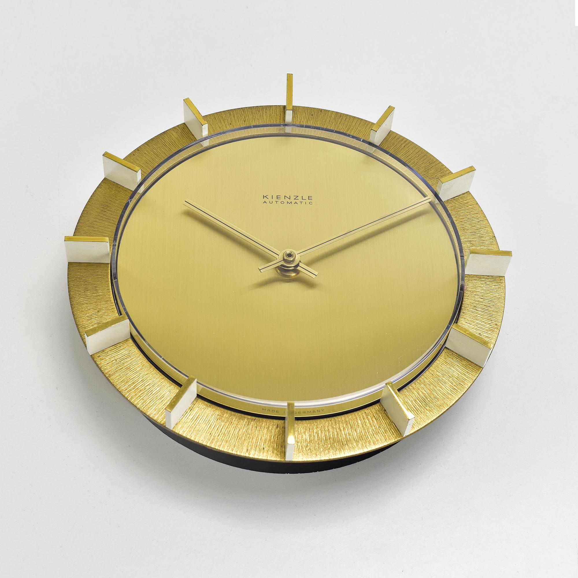 A highly decorative round gold-colored wall clock by Kienzle with an electric automatic movement. The edge of the clock is a cast brass round frame featuring raised, partially white lacquered indices made of flat metal with polished edges.