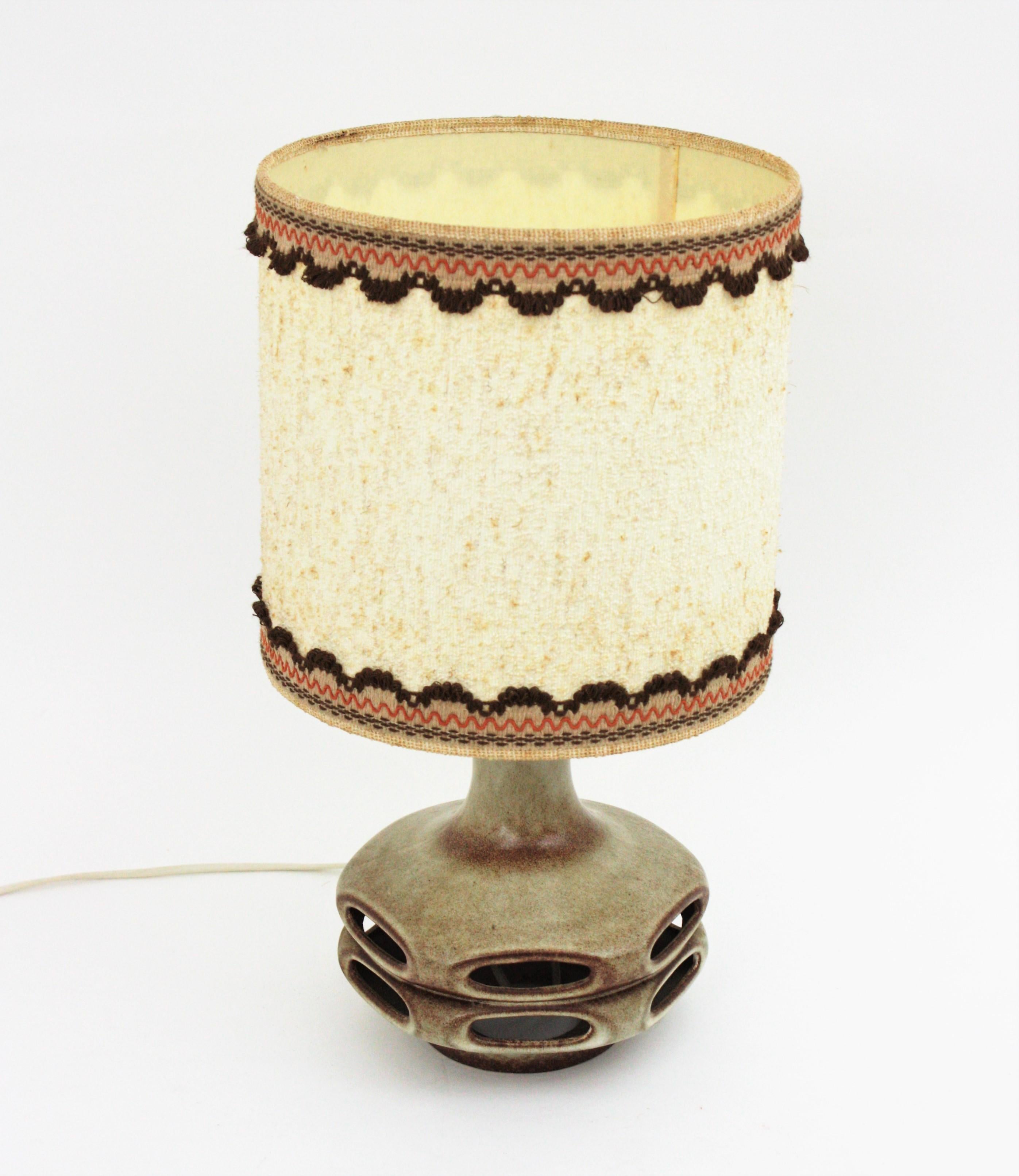 Mid-Century Modern ceramic table lamp with original textile lampshade. Germany, 1960s.
The base of the lamp has a design with holes that allows a highly decorative lighting effect.
Glazed ceramic in shades of brown.
Original fabric lampshade with