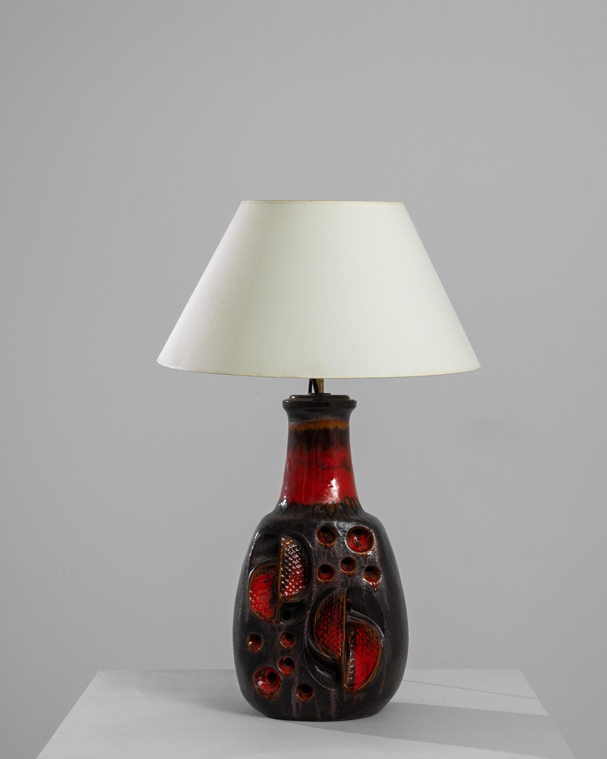 A ceramic table lamp from Germany, produced circa 1960. A beautiful example of Mid-Century German lava glaze ceramic, this tall table lamp, with its bright red tone flowing into brown black, glows like an ember. Deep half-spheres and semi-circles