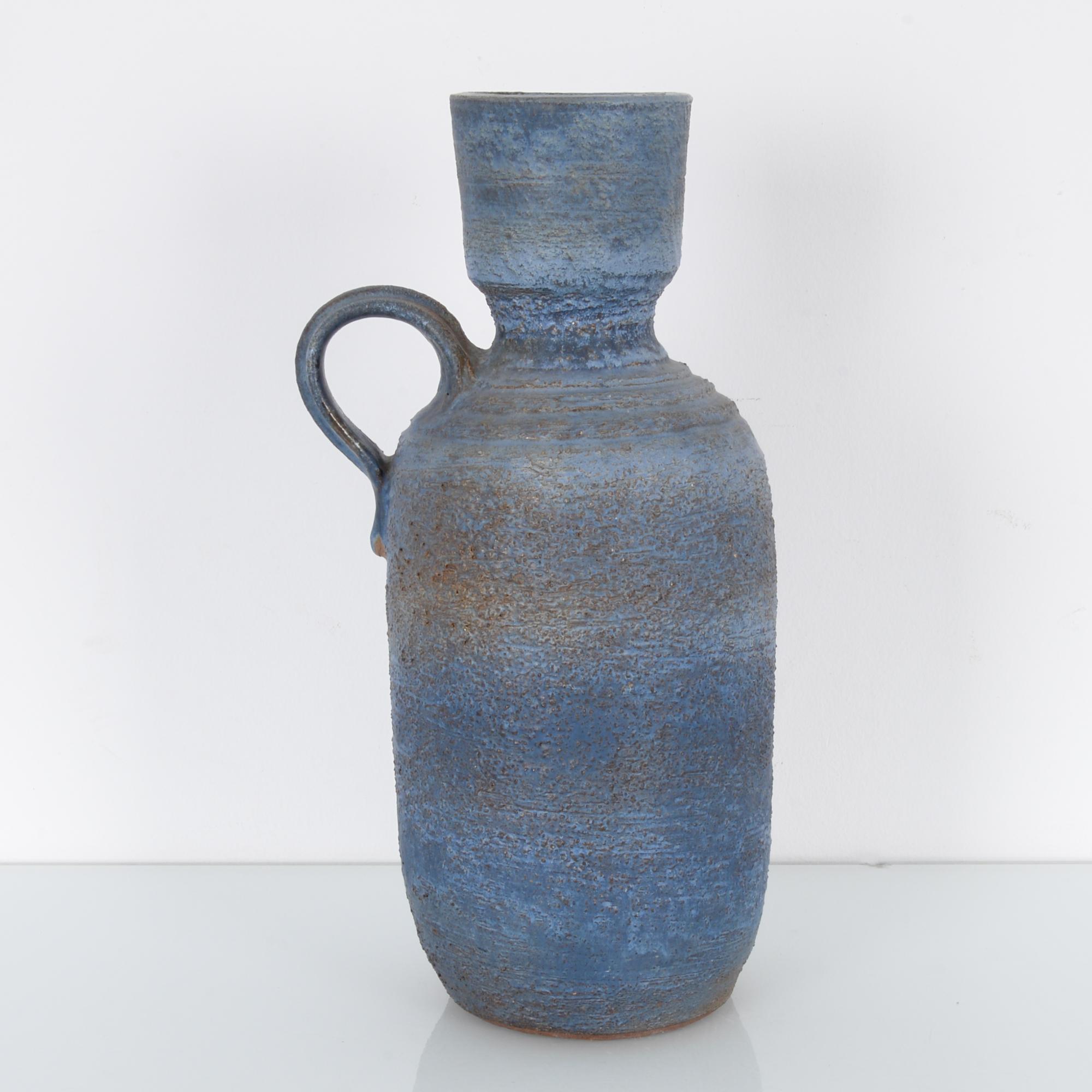This ceramic vase was made in Germany, circa 1960. Its blue and gray glazed, textured surface and the stepped shoulder display the experimentation characteristic of West German pottery from this era. A circular handle sits on one shoulder.