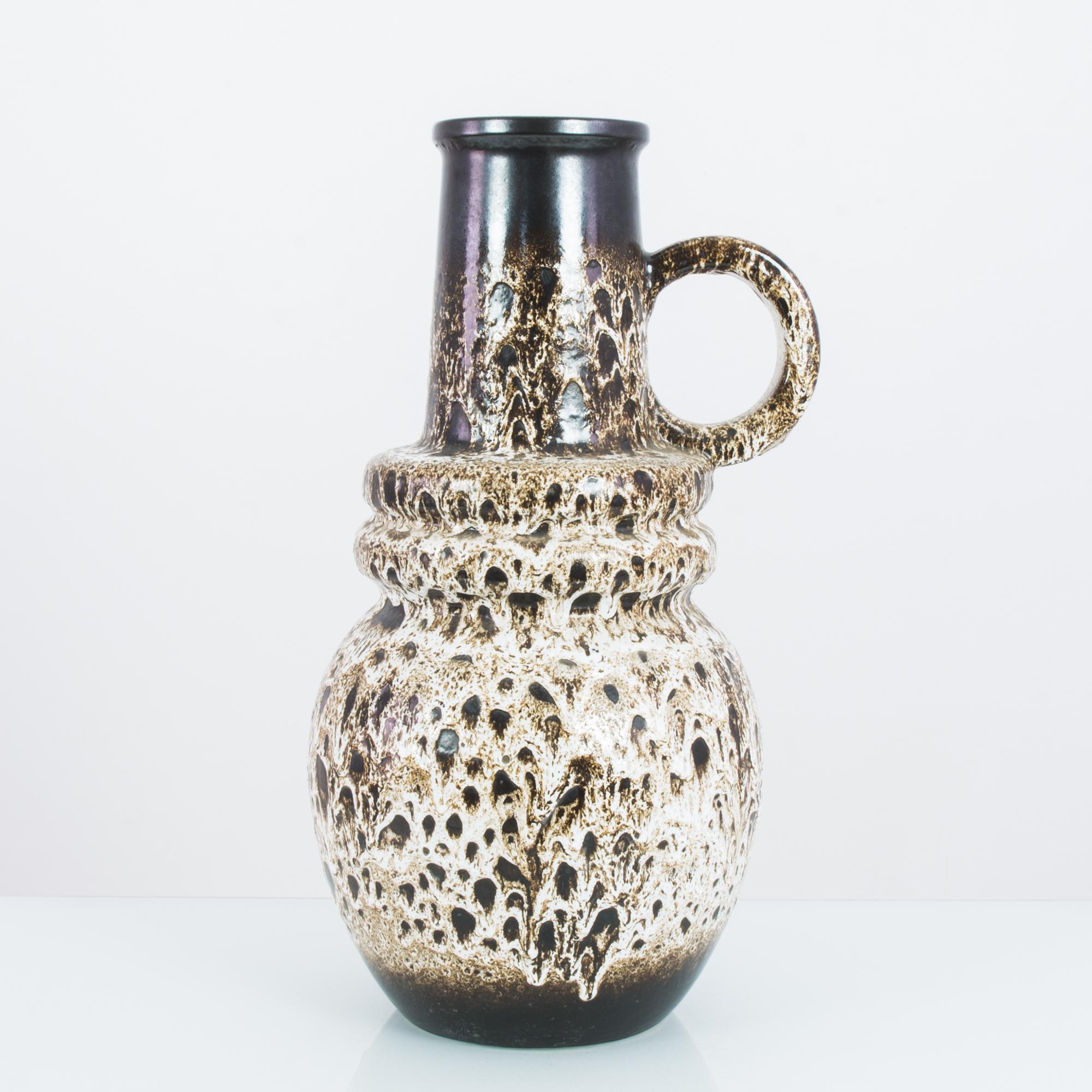 A ceramic vase from West Germany, circa 1960. A rounded and continuous shape: the bulb of the base ripples into ridges, then rises into a graceful funnel. The ceramic has a burnished tone, interrupted by a striking cream-colored glaze, which froths