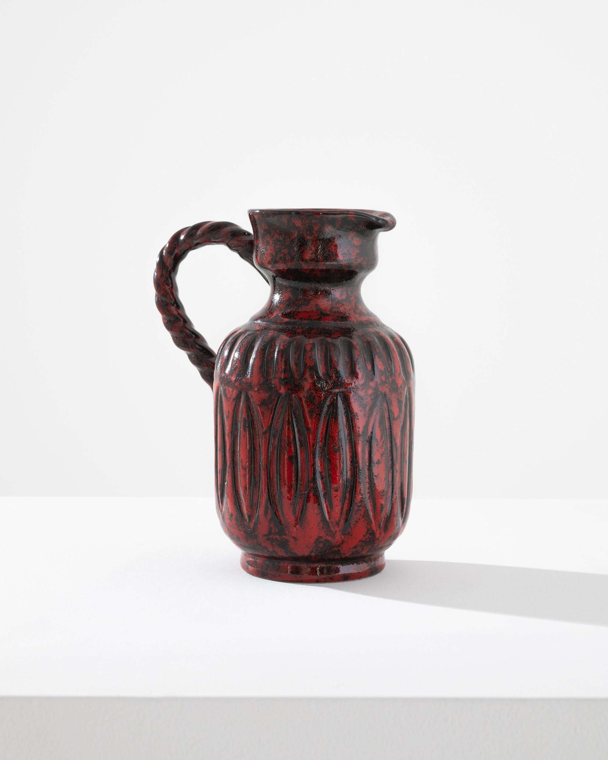 A vintage ceramic vase produced in Germany circa 1960, this pitcher displays all the emblematic qualities of the West Germany style, a unique regional trend. Exhibiting a thick volcanic glaze layered over graphic pressed patterns, the surface shines