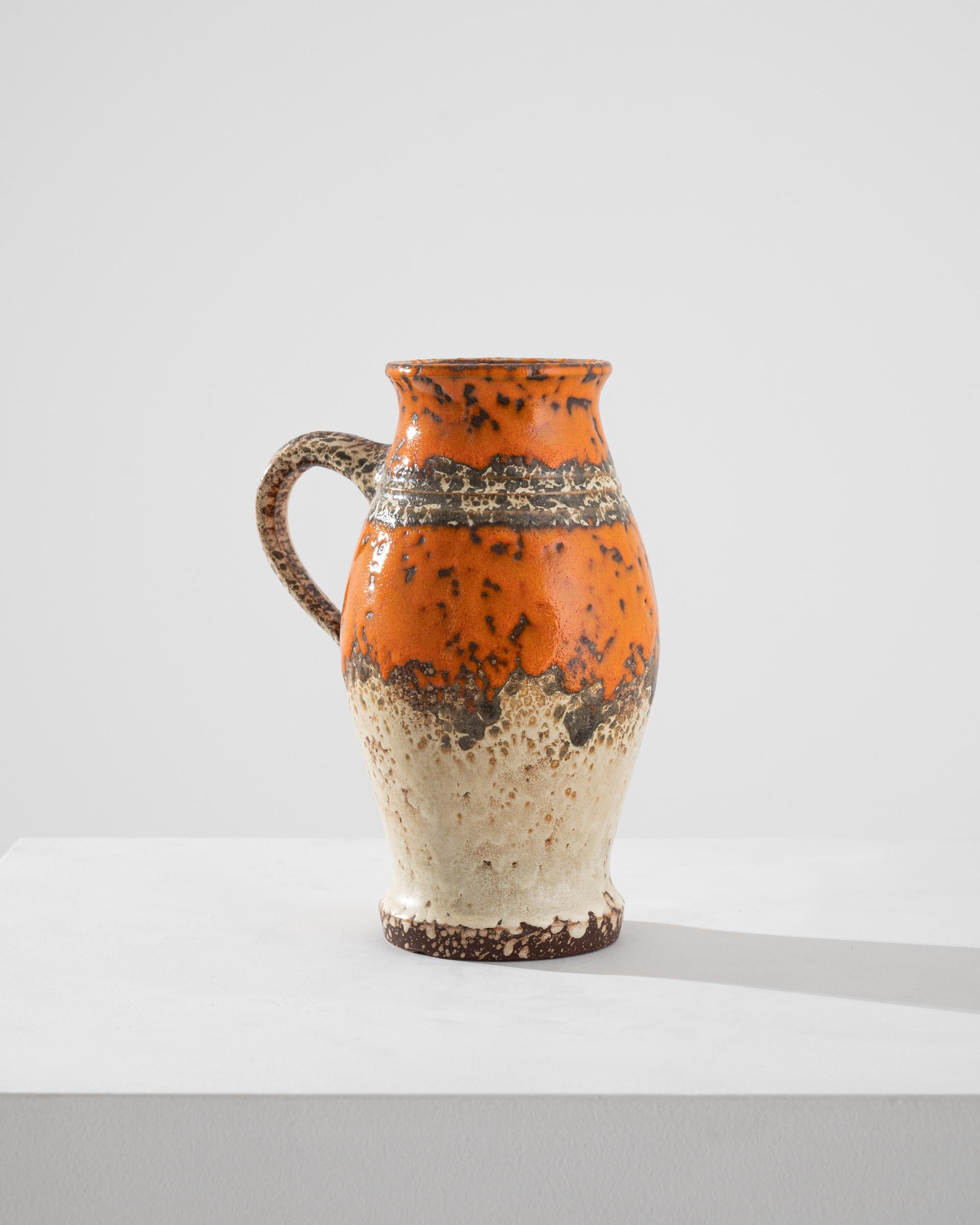 A vintage ceramic vase produced in Germany circa 1960, this pitcher displays all the emblematic qualities of the West Germany style, a unique regional trend. Exhibiting a thick volcanic glaze, the surface shines with a high key orange and titanium
