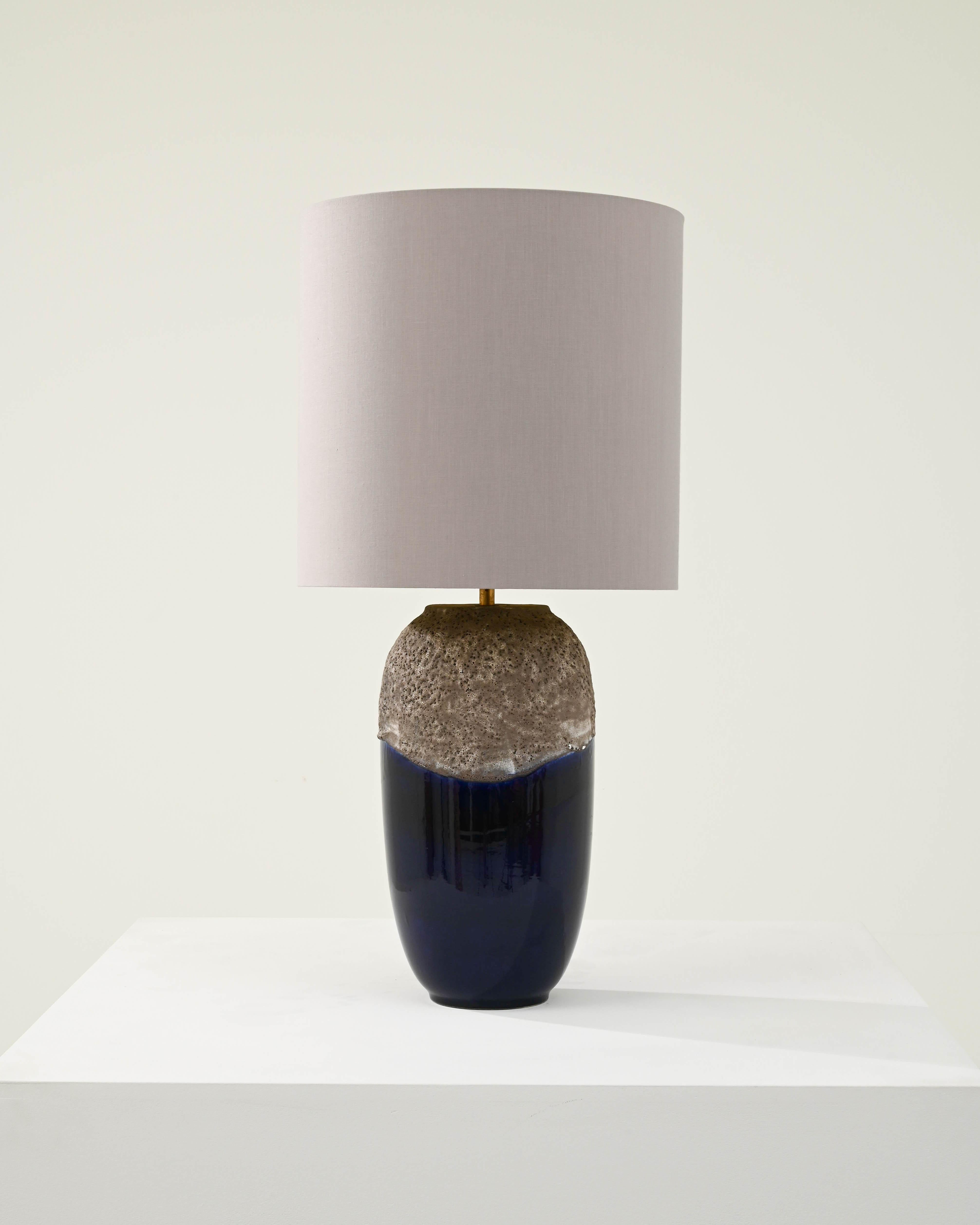 Designed in 1960s Germany, this vintage lamp showcases an alluring ceramic base with a captivating texture that envelops a polished deep blue surface, creating a striking contrast between the organic coarseness and refined sophistication of the