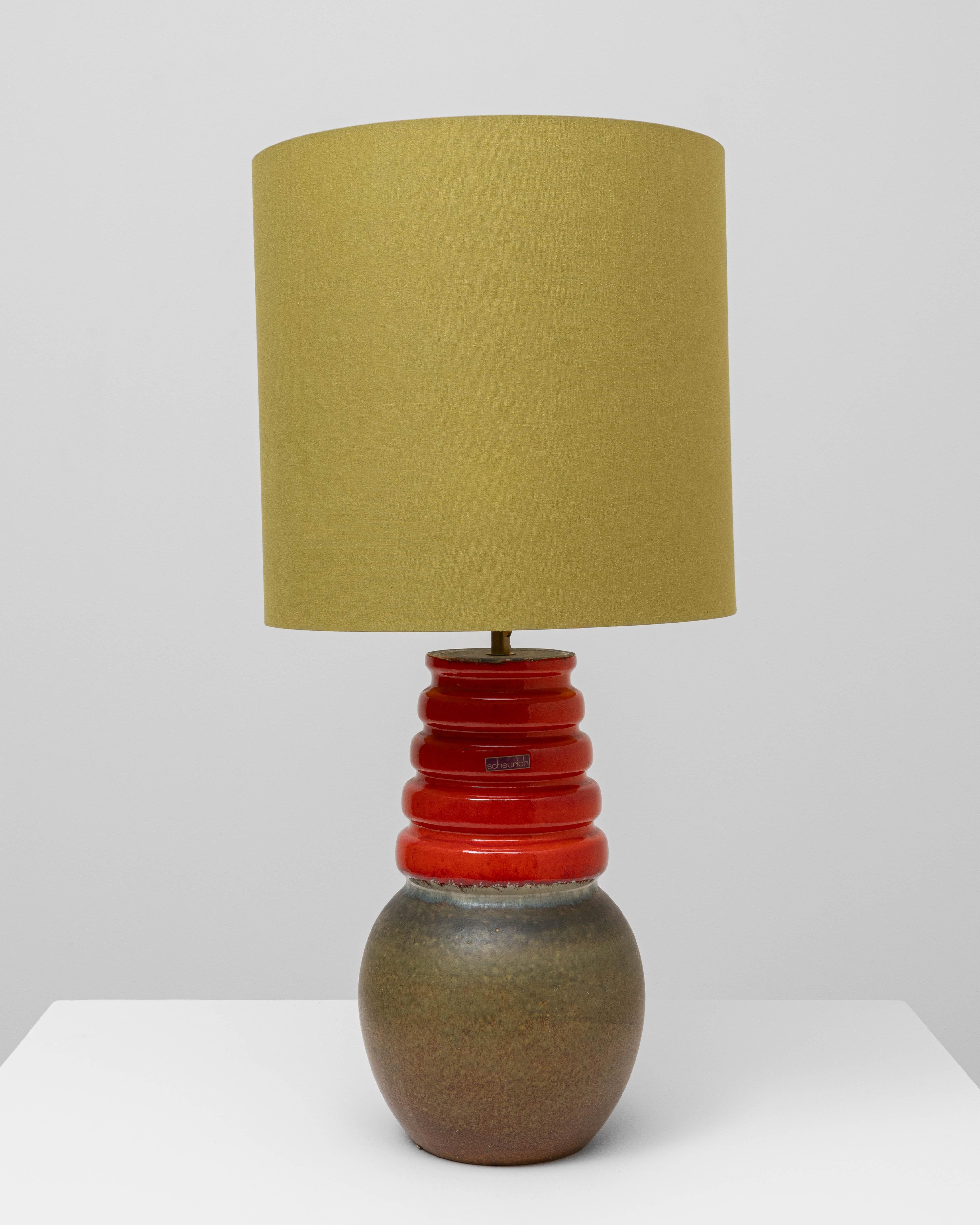 Cette lampe de table allemande en céramique verte et rouge des années 1960 présente une forme sculpturale saisissante qui allie des couleurs audacieuses à l'artisanat du milieu du siècle. La base passe d'une glaçure chaude aux tons olive à un