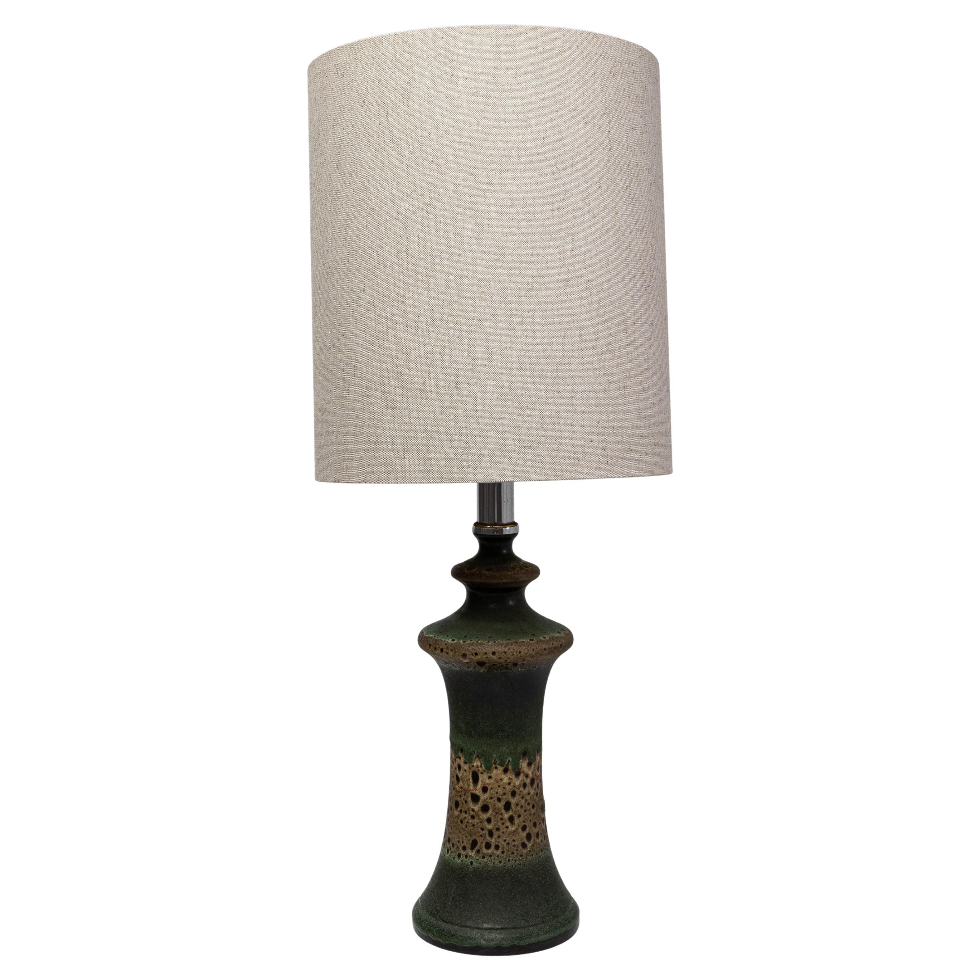 Esta lámpara de sobremesa de cerámica verde alemana de los años 60 presenta una silueta escultural combinada con un esmalte de rica textura típico de la cerámica de estudio europea de mediados de siglo. La forma alta y acampanada pasa de un verde