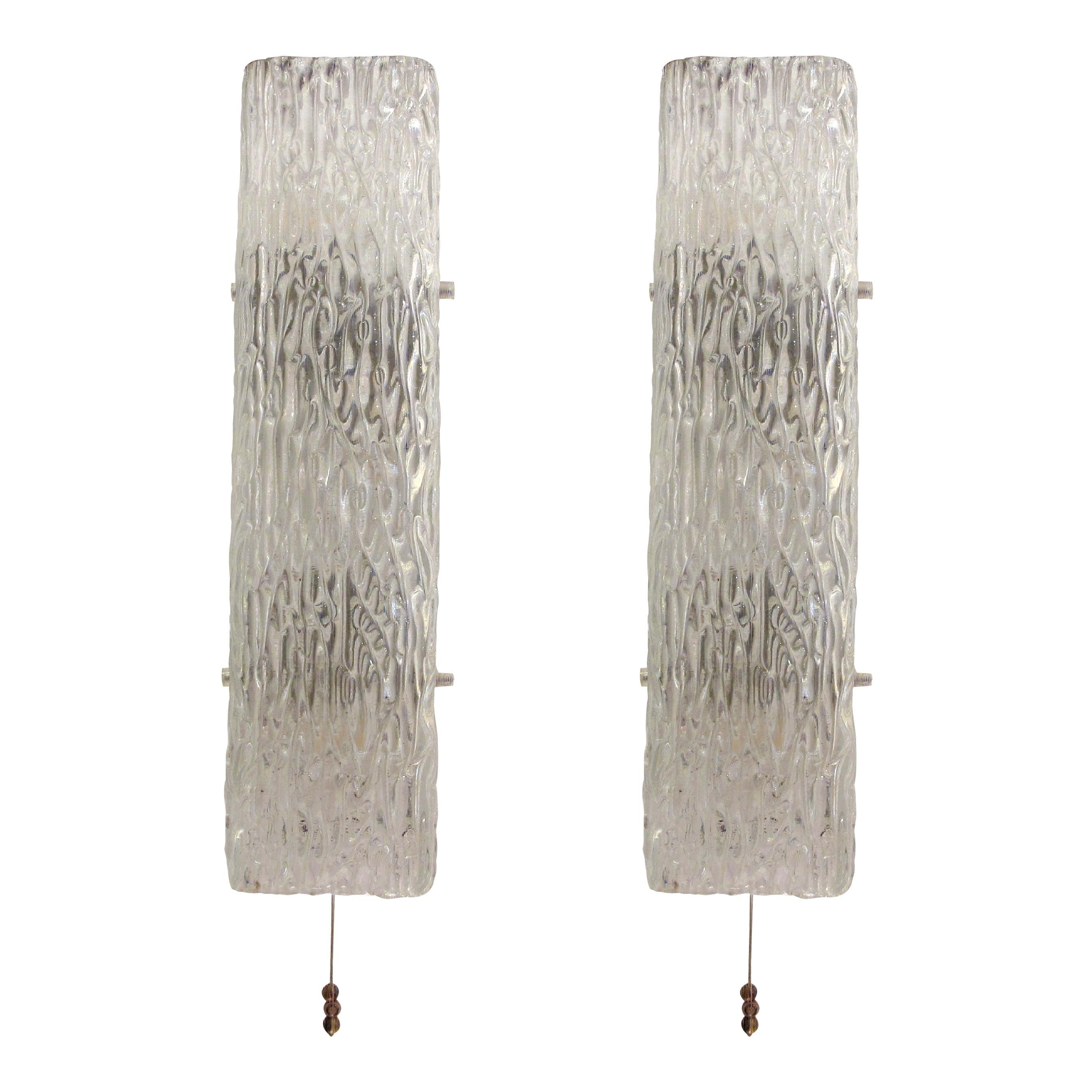 Si tratta di una coppia di appliques progettate da Kalmar Lighting negli anni '60 in Germania. Gli apparecchi sono caratterizzati da un vetro strutturato e modellato che ricorda le formazioni naturali di ghiaccio, conferendo loro un aspetto