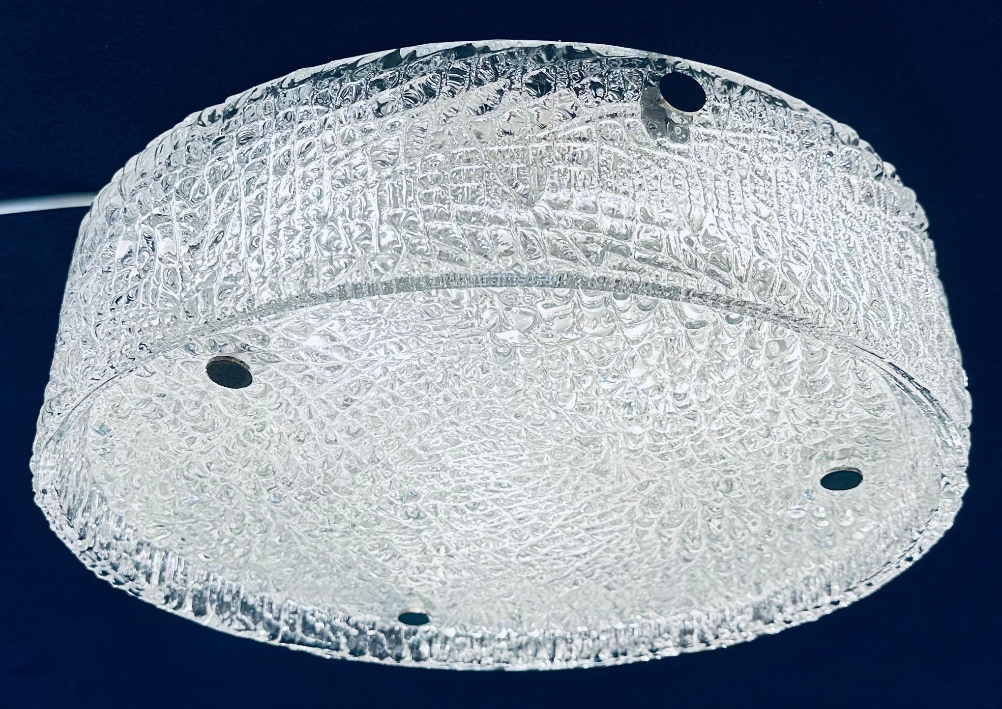 Deutsche Kaiser Leuchten aus den 1960er Jahren, strukturiertes Eisglas, bündig montierte Deckenleuchte. Die kreisförmige Grundplatte aus dickem, strukturiertem Glas wird mit drei Chromschrauben auf dem weißen Rahmen befestigt, um sie zu fixieren.