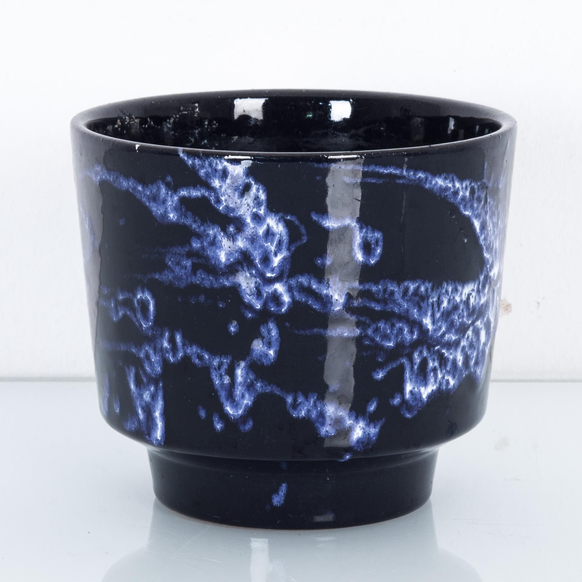 A ceramic vase from Germany, circa 1960. An open cup shape with a deep obsidian glaze. A current of indigo tendrils swirls over the black surface, an abstract pattern suggestive of night skies, nebulae or the mysteries of the deep sea. A modern and