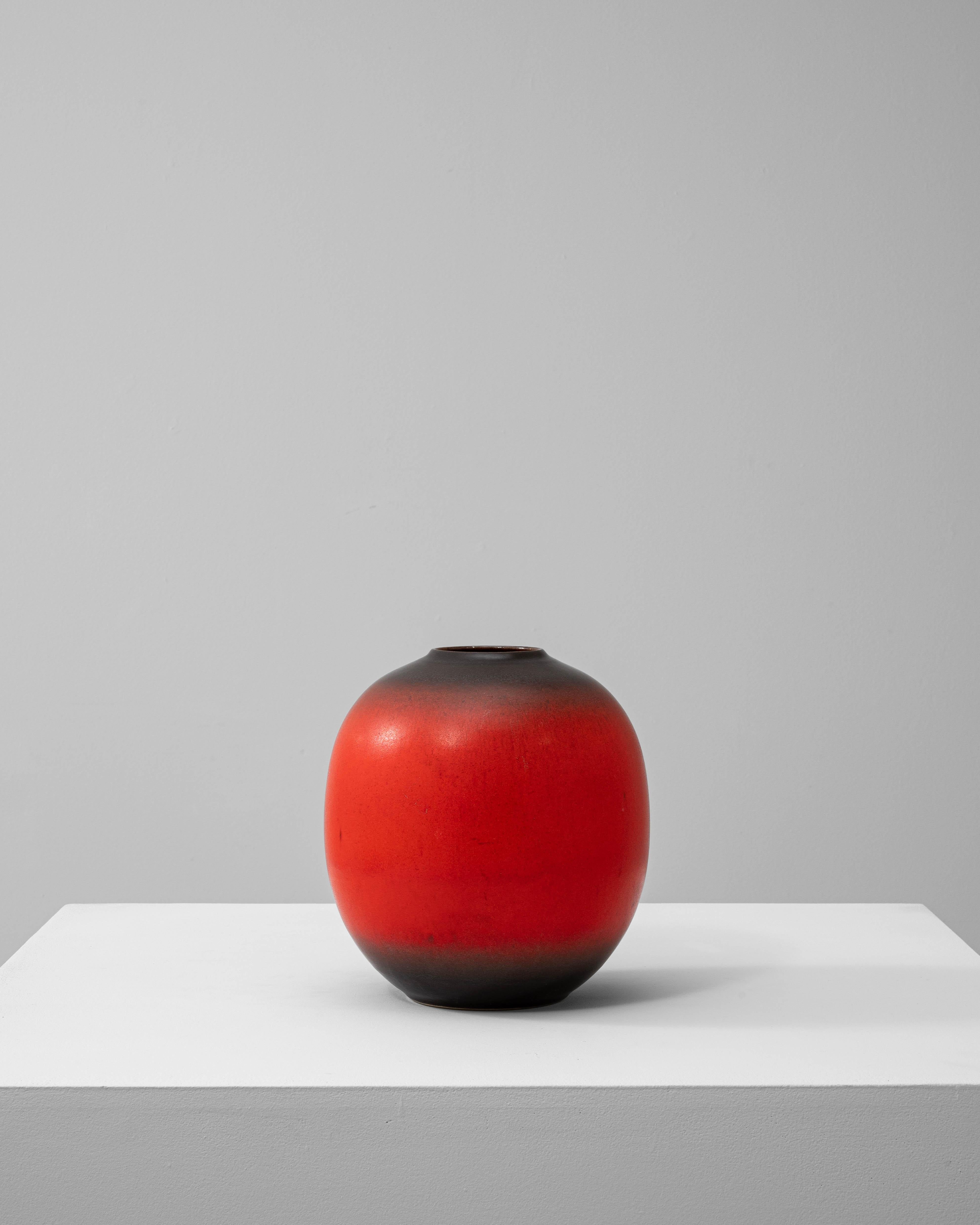 This 1960s German ceramic vase from West Germany embodies the bold, sculptural aesthetic characteristic of mid-century modern design. With a rounded, bulbous form and a striking matte glaze, the piece features a vibrant red body that transitions to