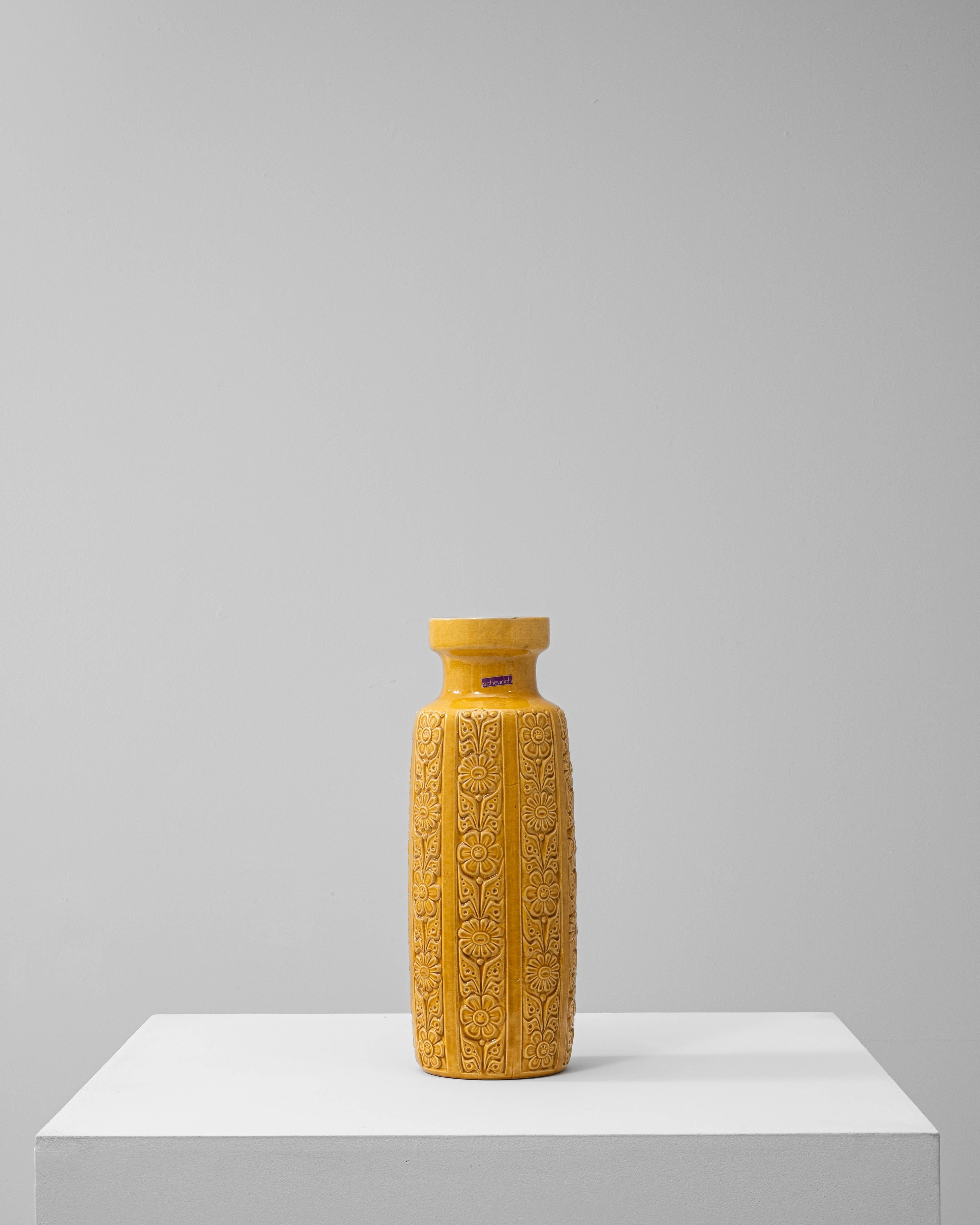 This 1960s German ceramic vase exemplifies the bold, textured style of mid-century “W. Germany” pottery, often referred to as Fat Lava ceramics. Finished in a rich mustard-yellow glaze, the piece features an embossed floral and geometric pattern