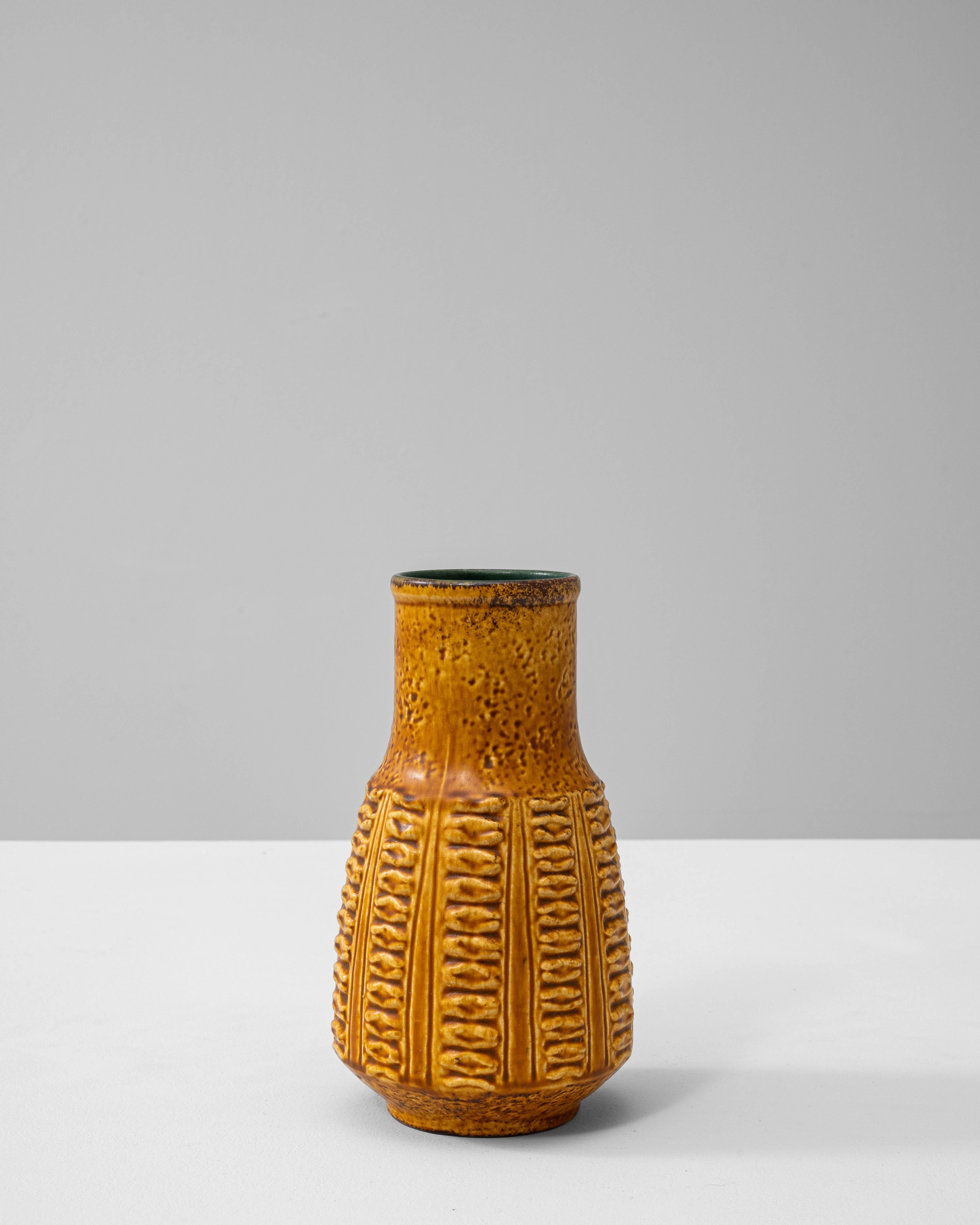 This 1960s German ceramic vase represents the distinctive craftsmanship of the “W. Germany” pottery era, celebrated for its bold glazes and textured surfaces. The vase features a warm ochre-yellow tone with a high-gloss finish and geometric relief