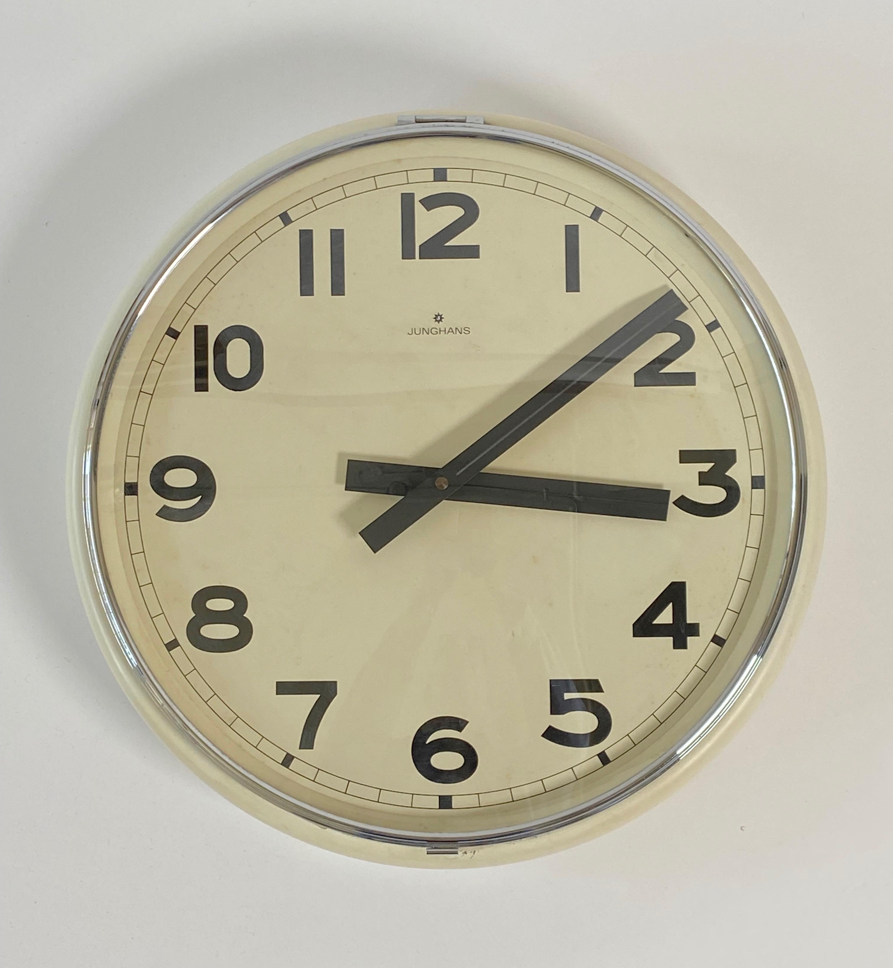 1960s Wall clock by Junghans of Germany with an off white cream colored case and a chromed frame glass lift up front cover. The hands are black with a raised center and squared off at each end. The Arabic numbers are big and bold and the over all