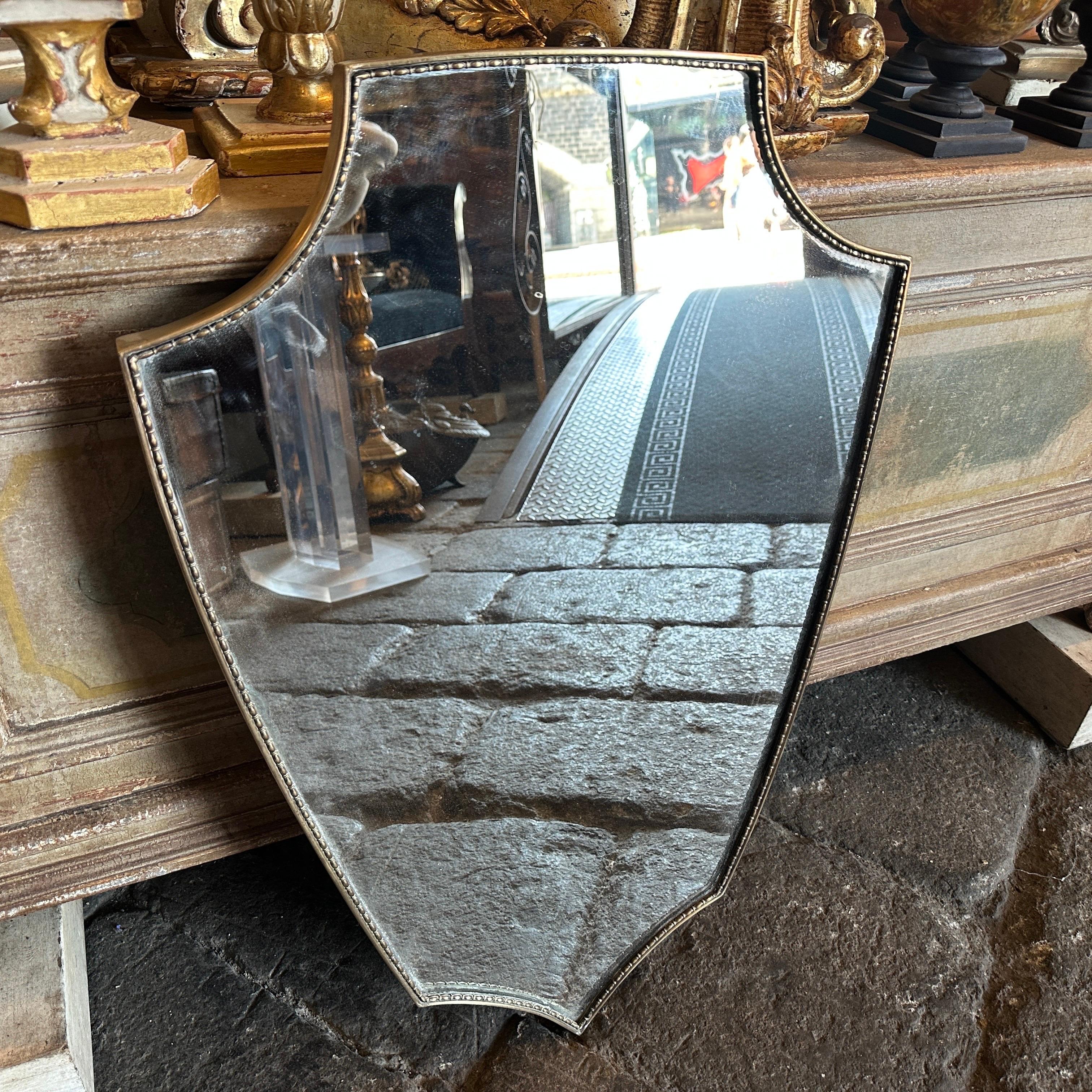 A shield shaped brass wall mirror designed and manufactured in Italy in the Sixties in the style of Giò Ponti, mirror is in good condition, brass in original patina. This shield wall mirror is a stunning piece of vintage decor that embodies the
