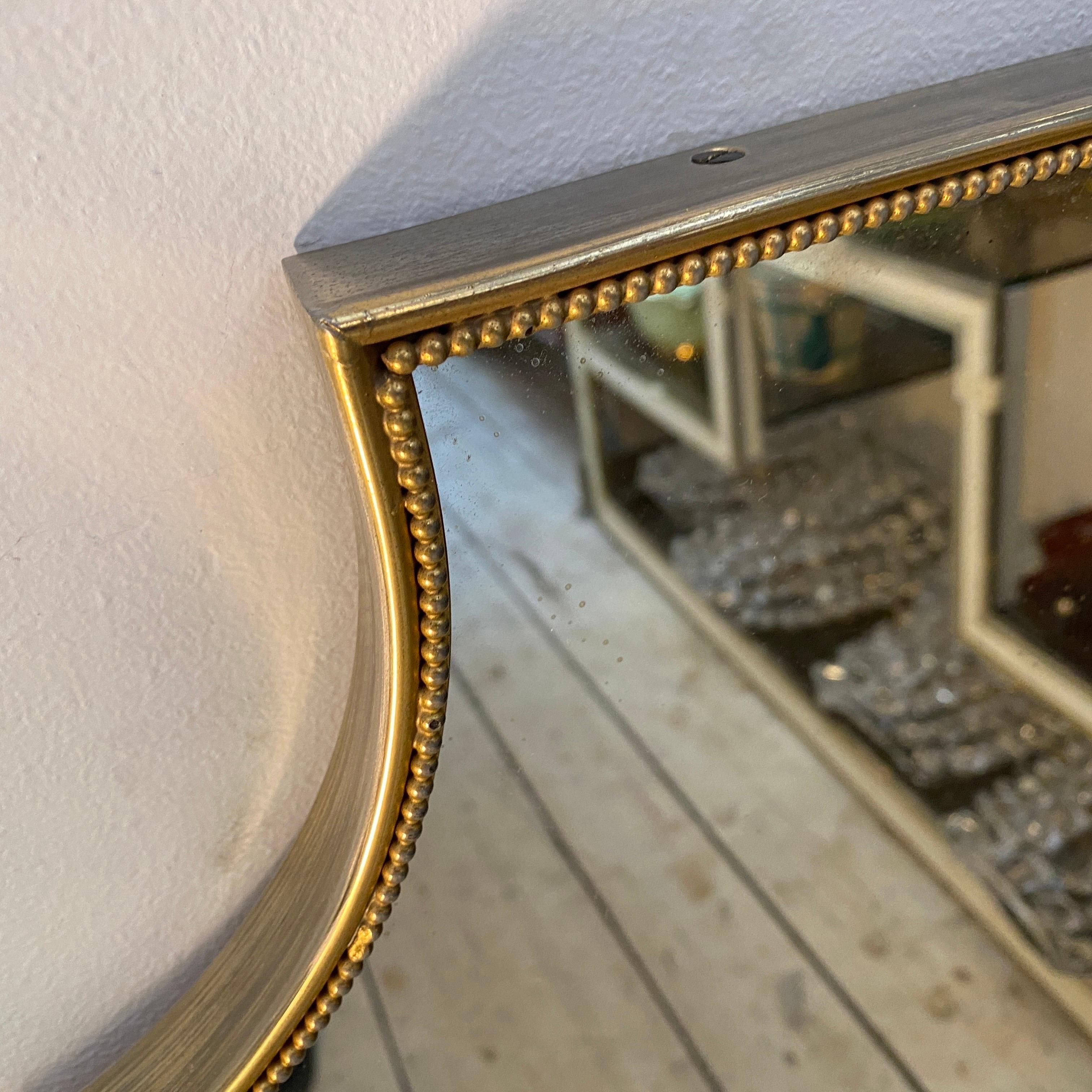 A Mid-Century Modern brass Italian mirror designed and manufactured in Italy in the Sixties in the style of Gio Ponti in very good conditions overall that have a sleek and elegant design with clean lines and a Minimalist aesthetic. It has a shield