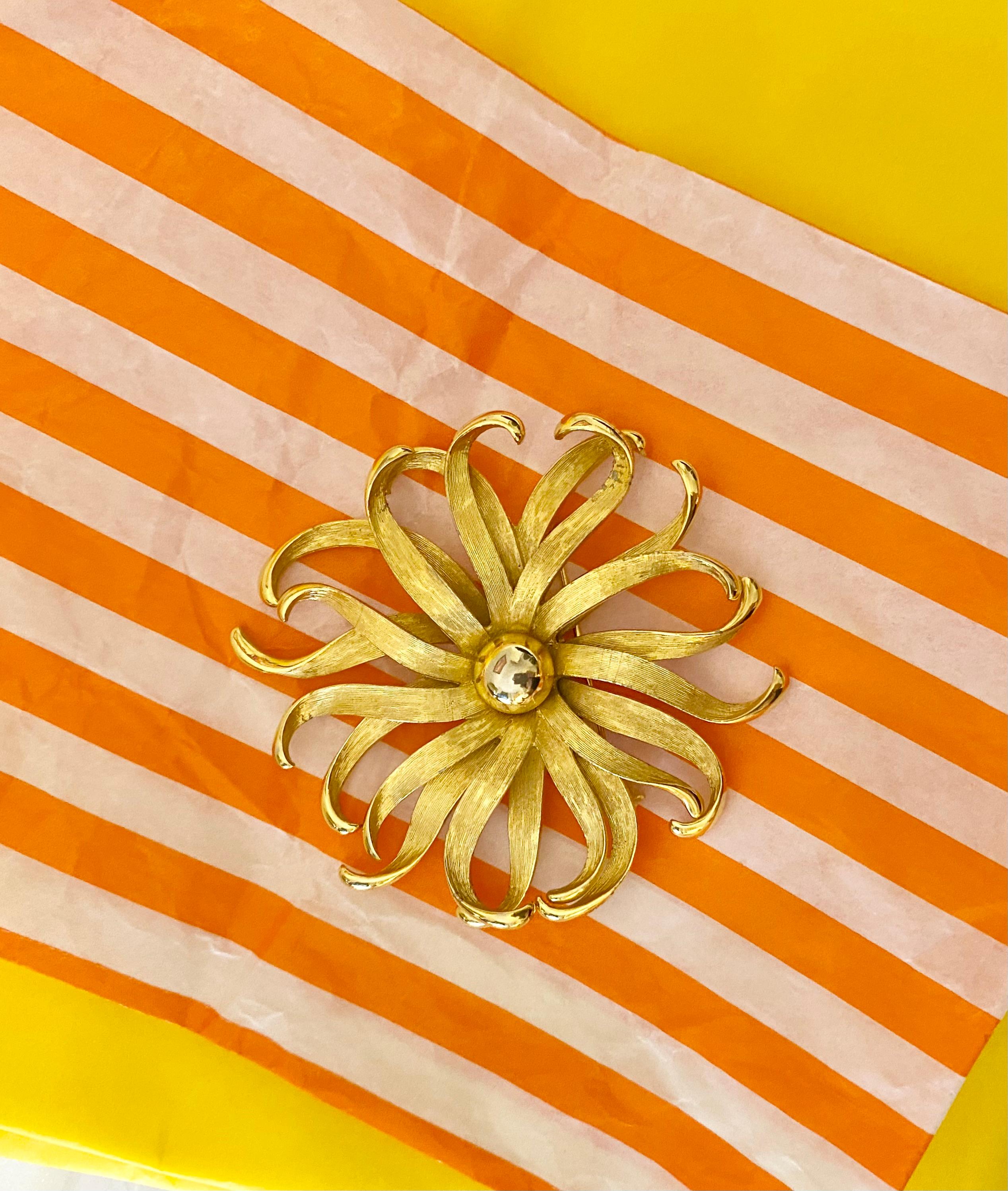 Broche Givenchy de los años 60 diseñado en forma de flor abstracta escultural, presenta pétalos de metal cepillado en tono dorado con suaves curvas y un centro de cristal facetado que añade un sutil juego de luces. La pieza está rematada con un
