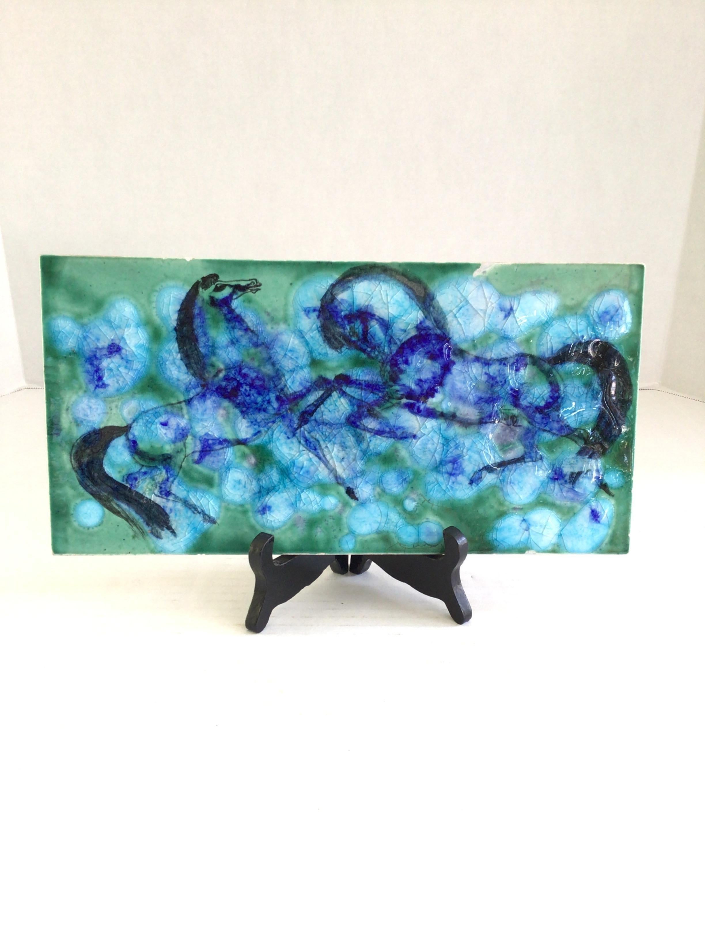 Piastrella smaltata e dipinta degli anni '60 raffigurante due cavalli che si stanno allevando
Superficie rialzata
Blu brillante, verde brillante, blu scuro 
Crepe nello smalto
Lievi scheggiature sul bordo (come mostrato nelle immagini)

Supporto in