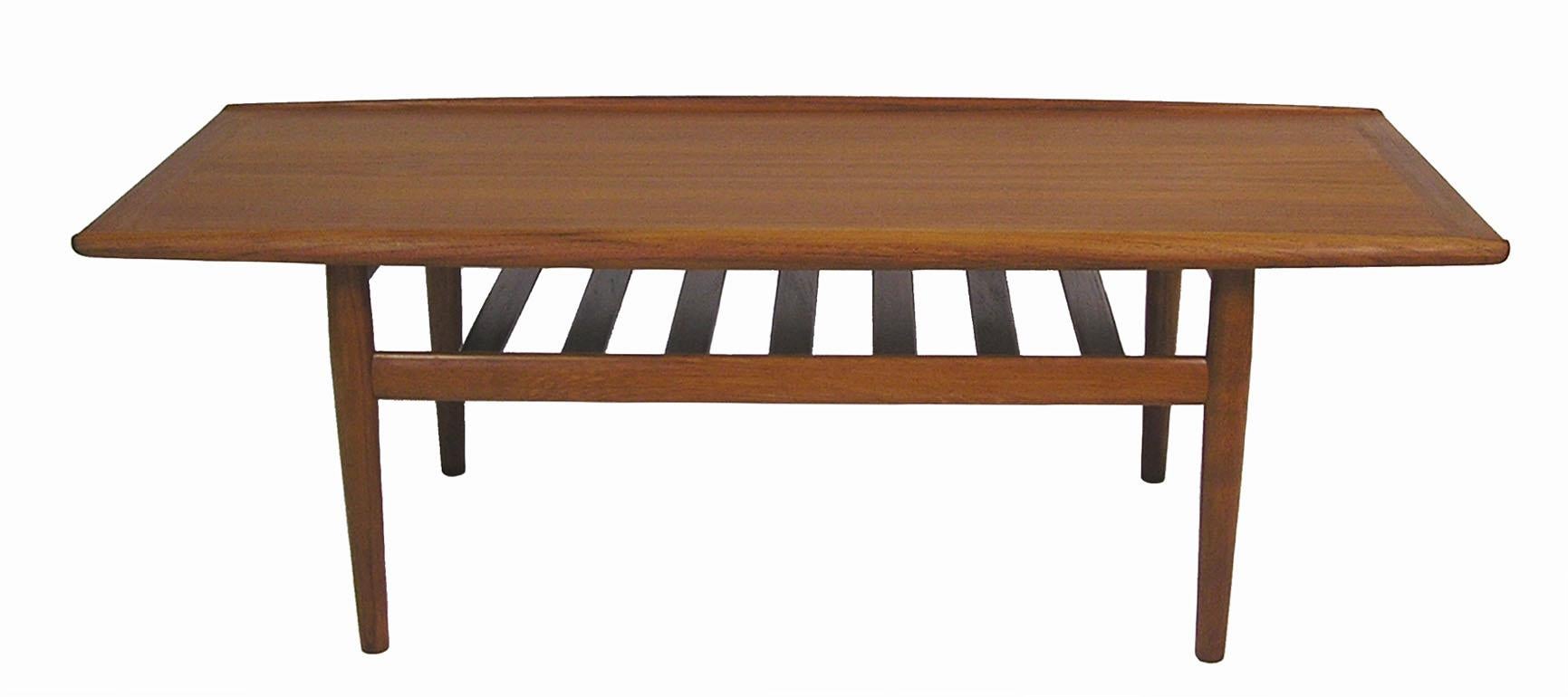 A gorgeous teak coffee table from the 1960s designed by Grete Jalk for Glostrup Mobelfabrik of Denmark. Beautiful craftsmanship throughout featuring a sculptured raised lip and slated lower shelf. Overall excellent condition with a newly refinished