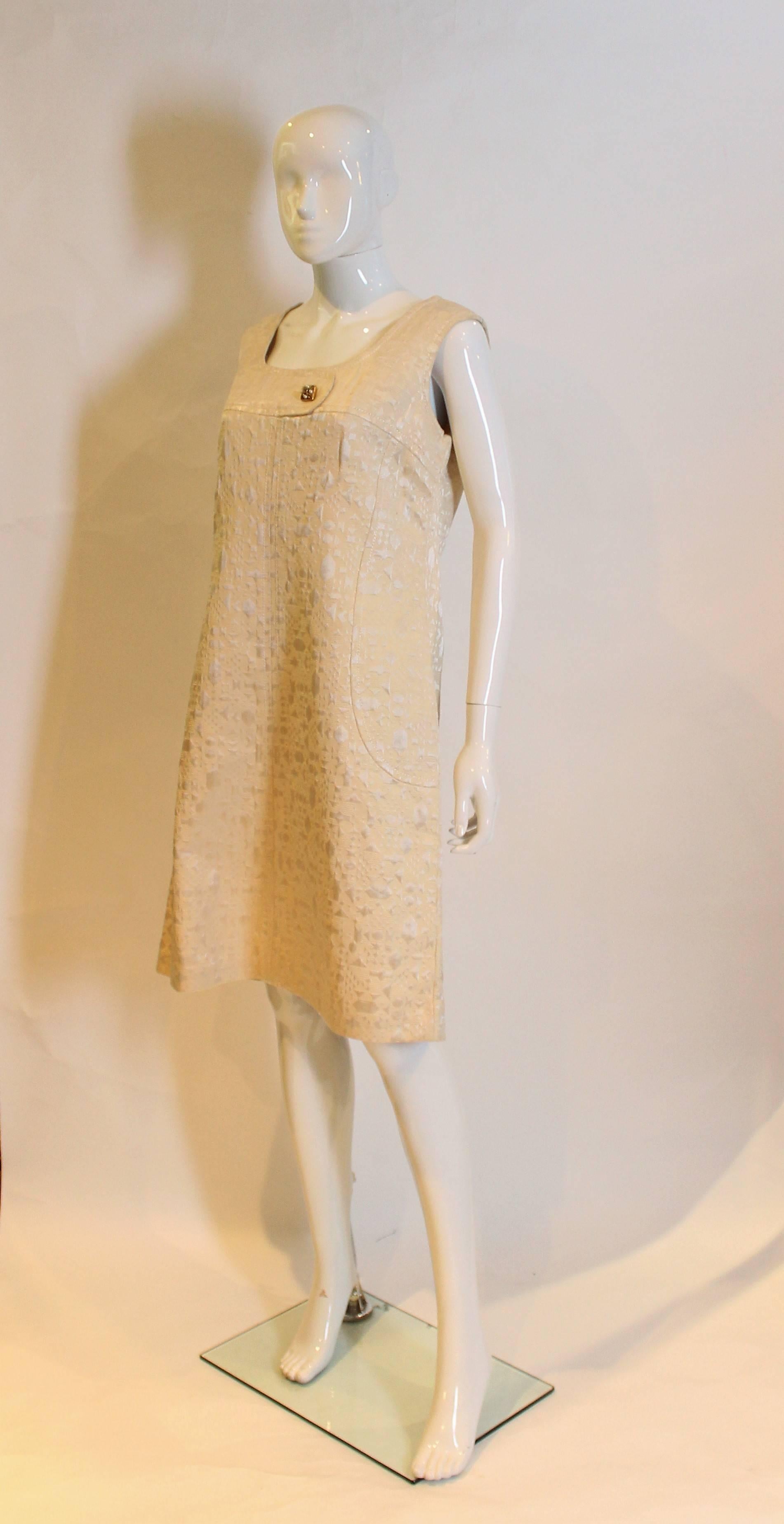 A chic shift dress from the 1960, ideal for a city wedding. The dress is made of a gold broacde like fabric with a deep square neckine and no sleeves. It has a zip opening at the back and an A lline skirt .