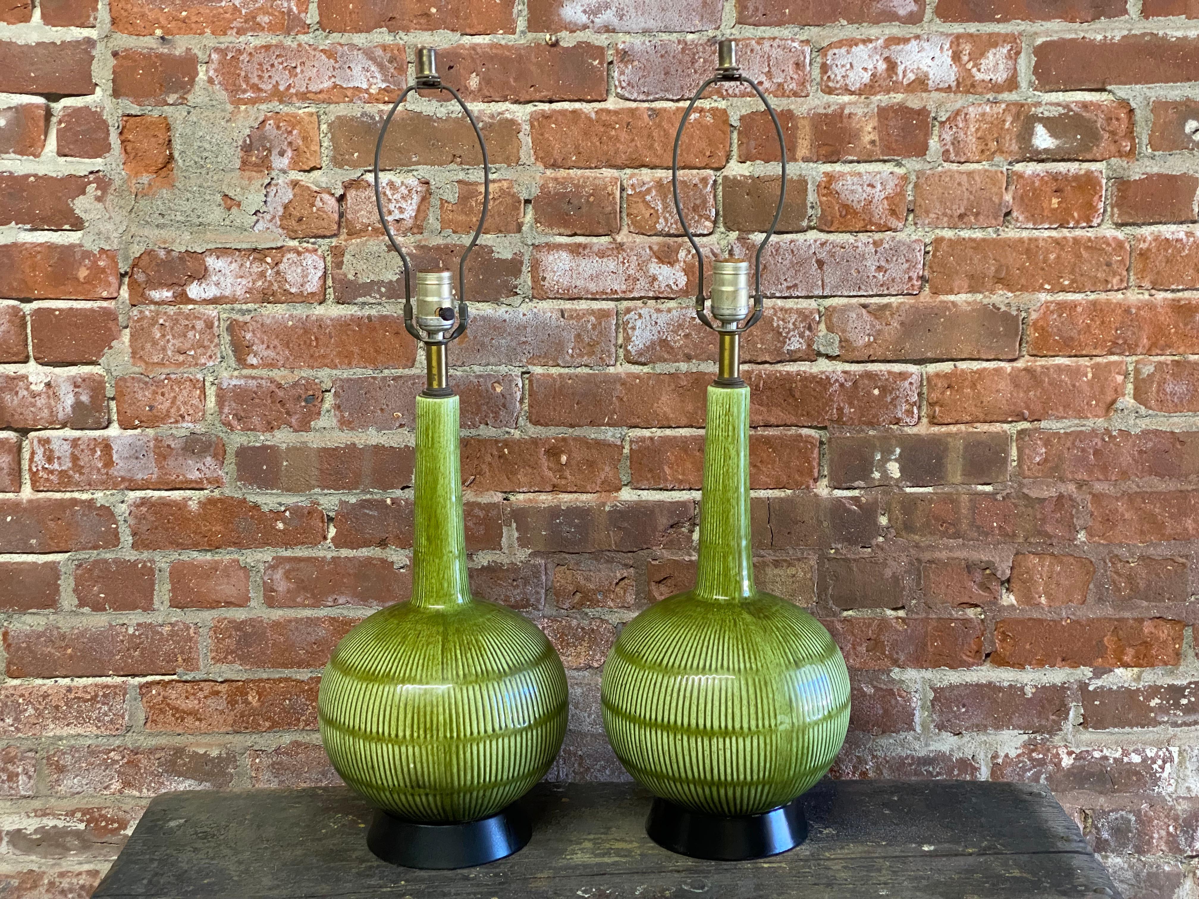 A fine pair of green glazed cast ceramic table lamps. Black metal bases. Asian inspired form. Circa 1960. Old working wiring. Good overall condition with no cracks, hairlines or restorations. Some light crazing and glaze pops. The bases look like