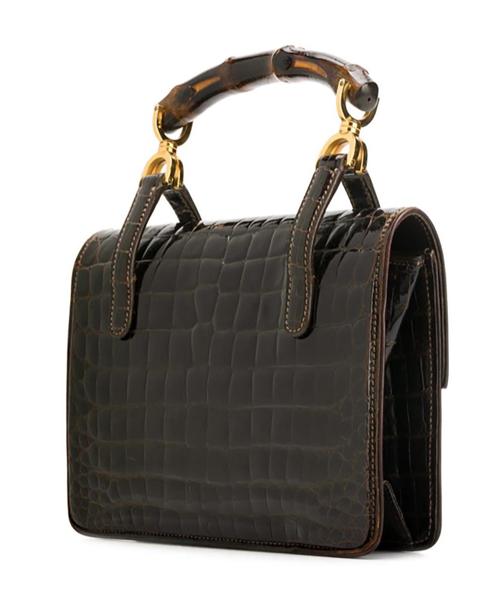 1960s Iconic Gucci dark brown crocodile leather Bamboo handbag featuring a varnished finish, gold-tone hardware, an internal slip pocket, an internal zipped pocket, an internal logo stamp, a front slip pocket, a Bamboo top handle and a foldover top