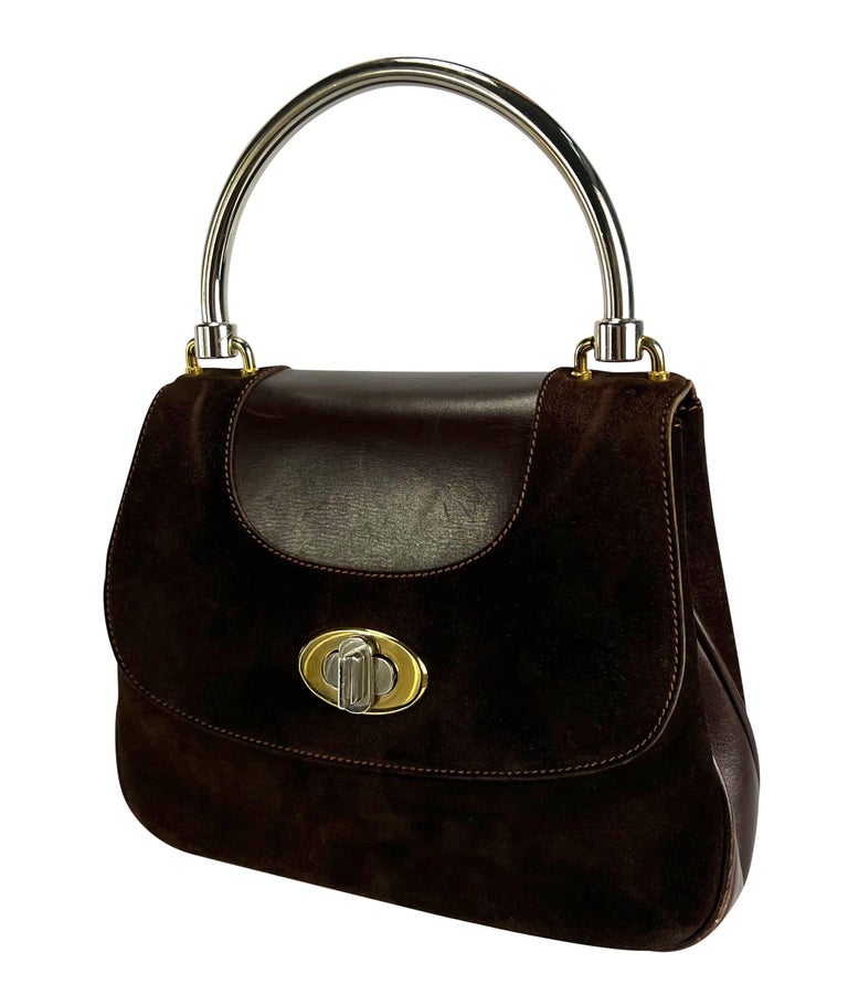 TheRealList presents: a vintage 1960s Gucci structured leather top handle bag. This classicly designed bag features a dual-tone metal handle and closure. The brown suede perfectly contrasts the shine of the two-tone hardware. Grab this classic piece