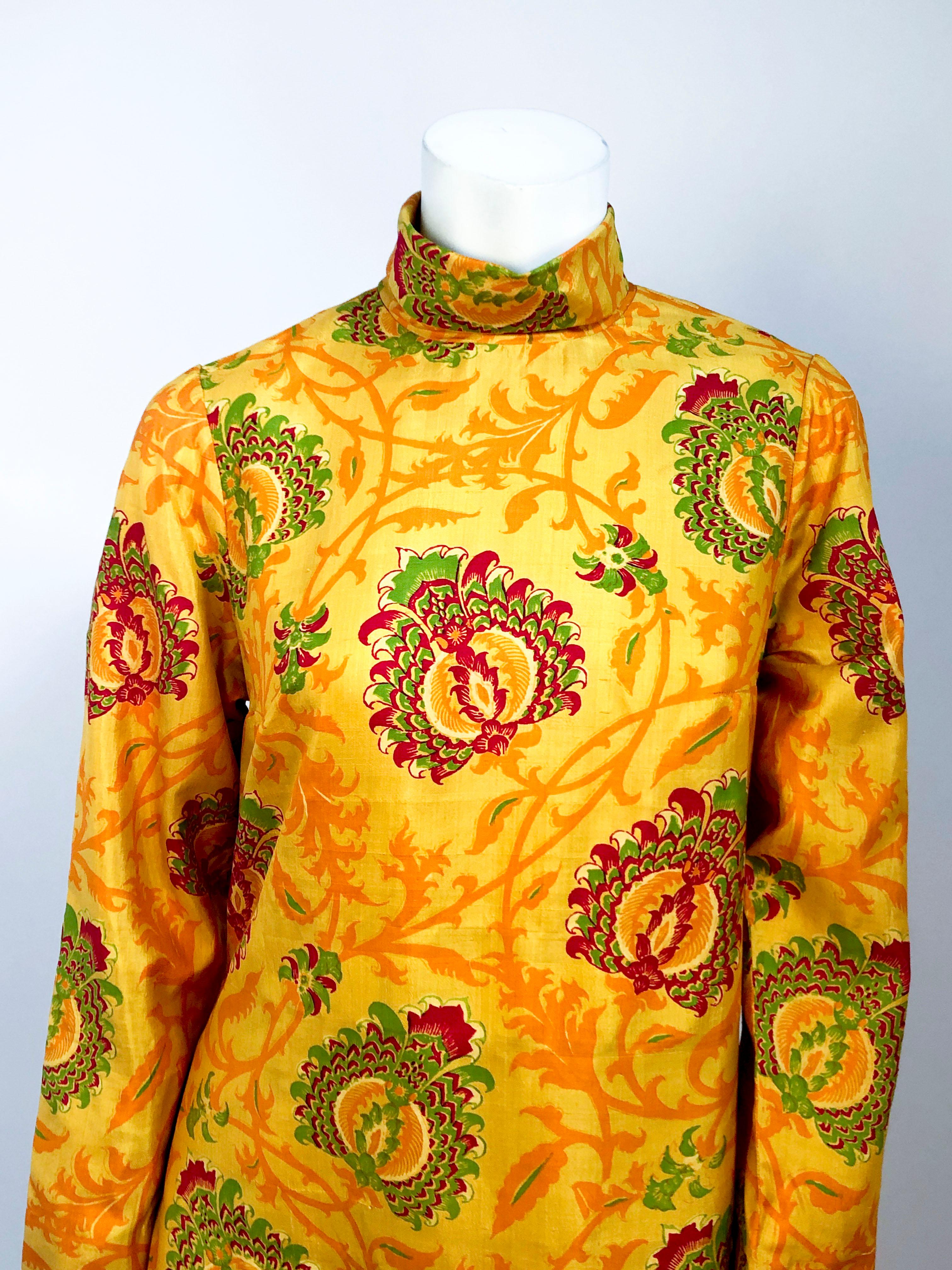 Ornate printed silk full length tunic in neon oranges, reds, and greens with long sleeves, high neck, and high side vents. the Pants have a complementary boarder print that extenuates the wide legs and high waist. Due to the vents on the sides of