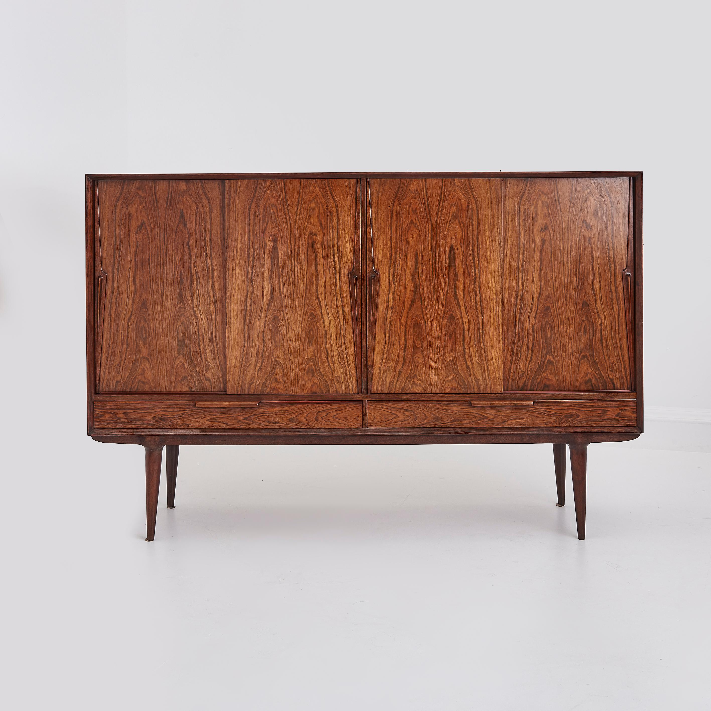 This sideboard is a prime example of mid-century Danish design. 

Crafted from beautifully grained rosewood, this piece features clean lines, a warm natural finish, and elegant sculpted handles, designed by Gunni Omann for Axel Christensen,