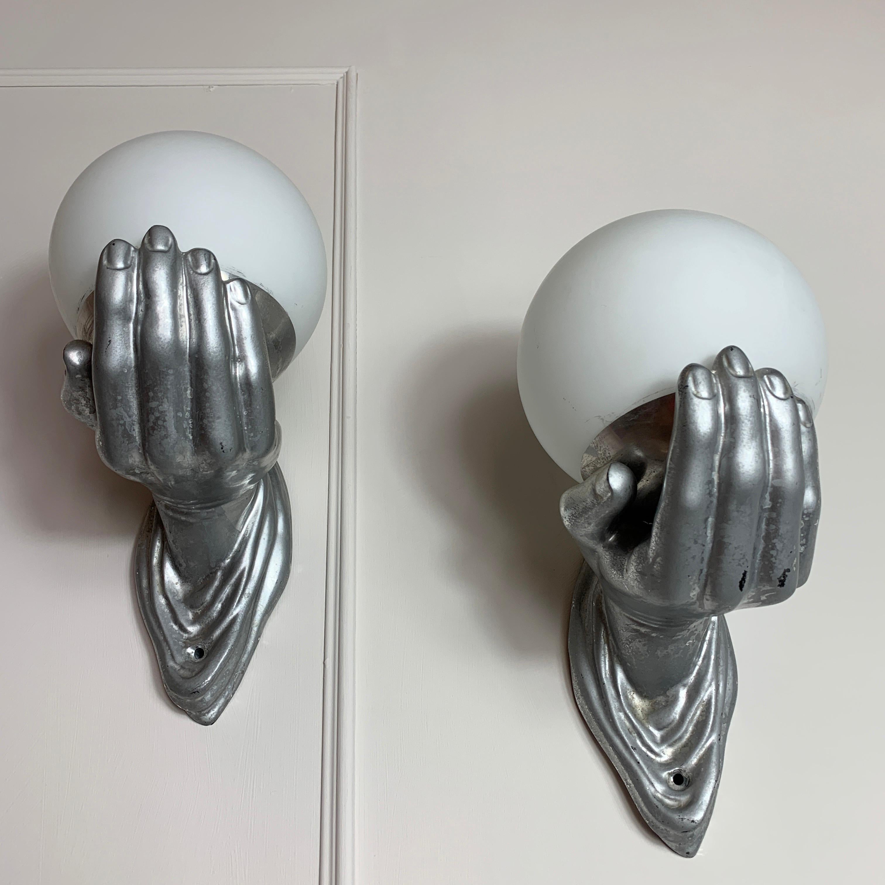 1960s hand and globe wall lights, in the manner of Arlus, France.
This is a great looking pair of wall lights in the design of hands holding globes.
The hands themselves are in bronze with glass globe shades, these shades are held in place with