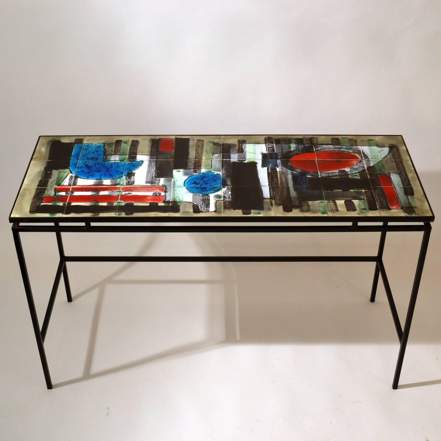Modernist desk or console table with hand painted tiled top in abstract design with splashes of bright colors red and blue on a suspended black metal frame, signed by Juliette Belarti, Belgium, circa 1960.
  