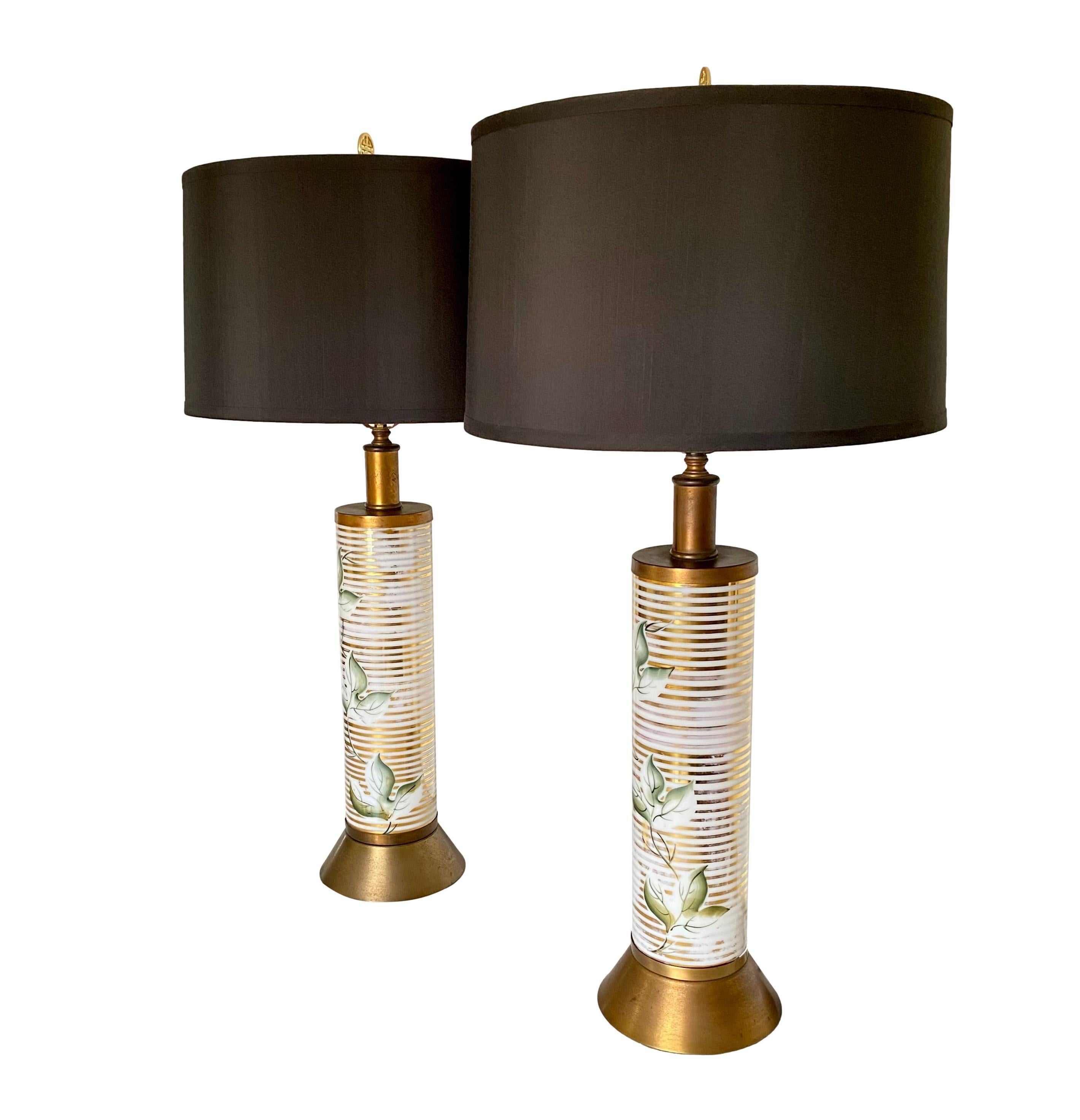 A vintage 1960's pair of ceramic pillar lamps in good working condition with black silk-blend drum lamp shades. Hand painted foliate motif over horizontal bands of gold leaf with brass base/details and Asian style medallion finial.

Dimensions: